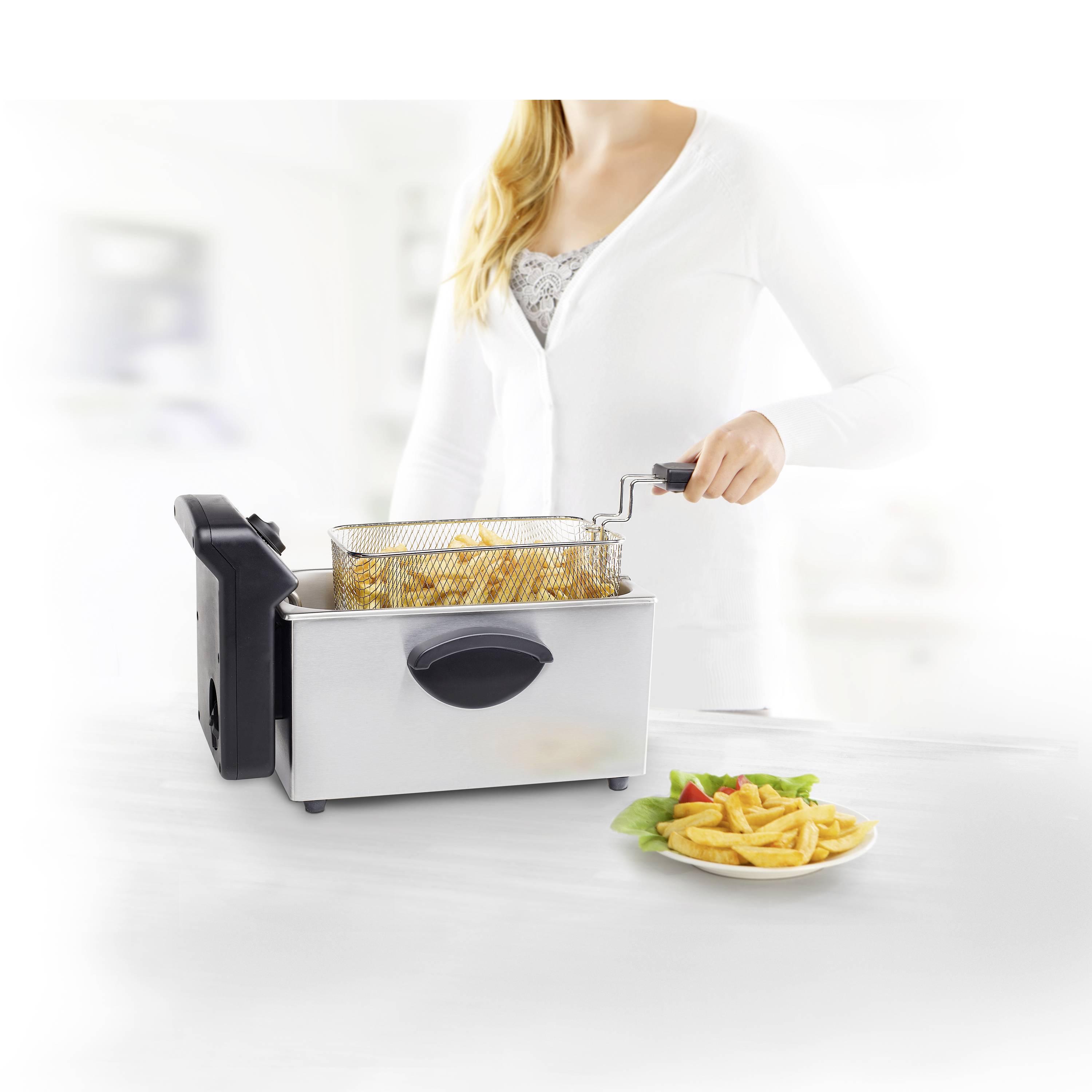 Une personne sort un panier de frites frites d'une friteuse moderne en acier inoxydable. À côté se trouve une assiette de frites.