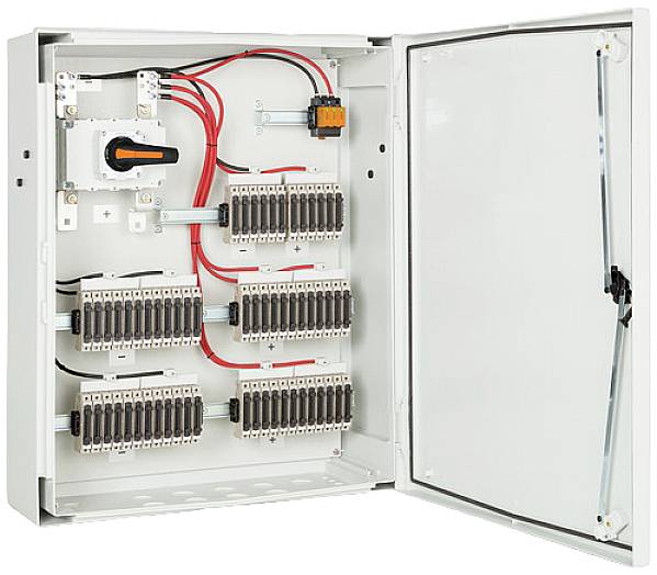 Armoire électrique ouverte avec plusieurs rangées de fusibles et de connexions de câbles. Un interrupteur principal est situé à gauche.
