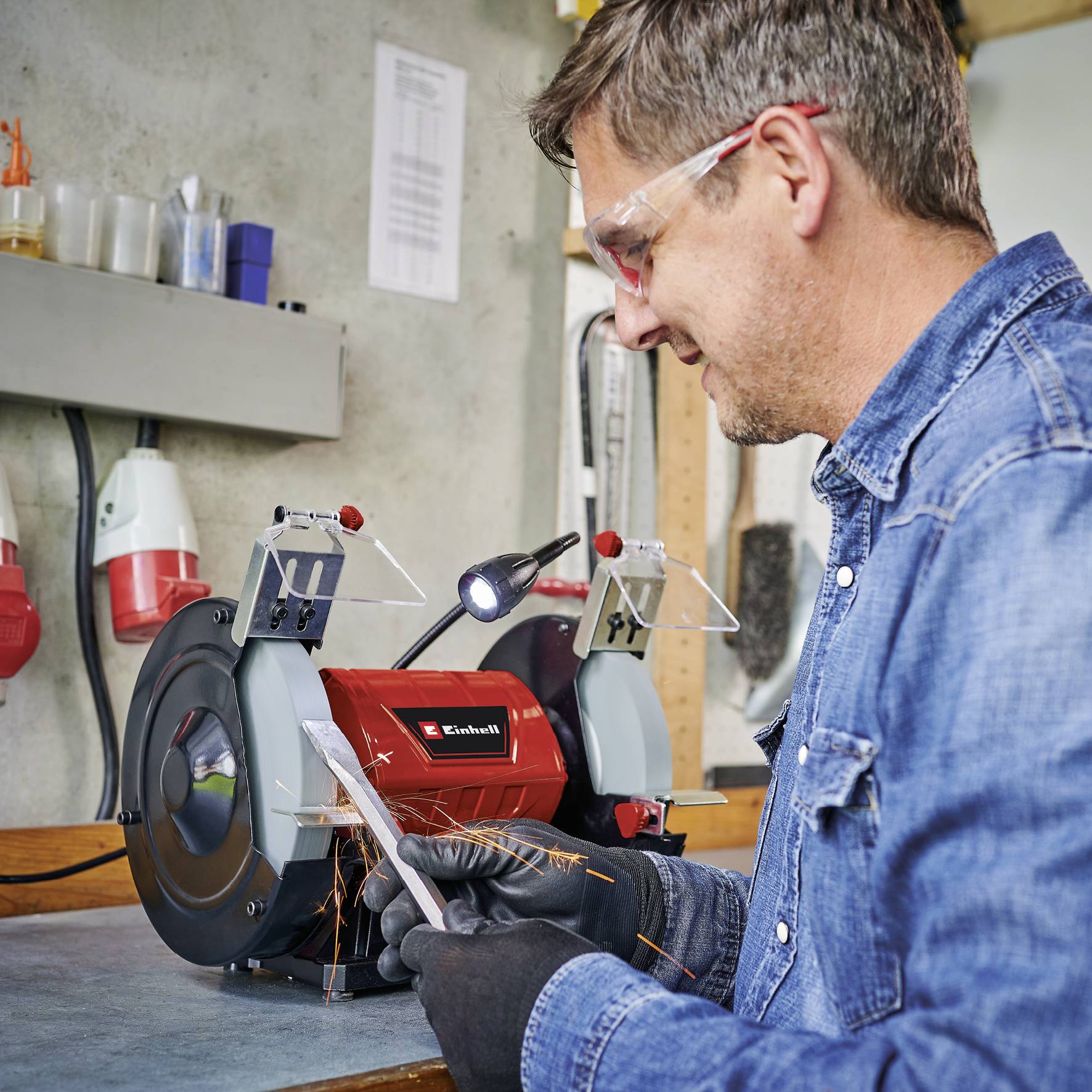 Un homme porte des lunettes de protection et travaille sur une meuleuse dans un atelier. Il tient un morceau de métal dans sa main.