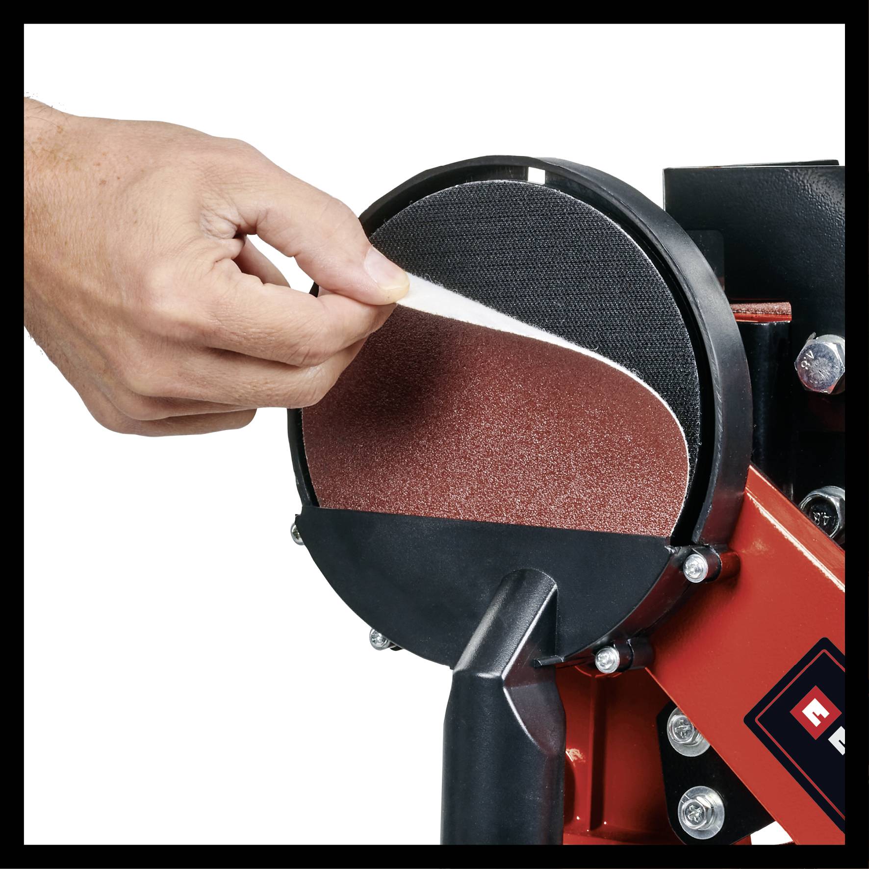 Une main retire un disque de papier abrasif d'une machine à poncer rouge et noire, illustrant le processus de changement.