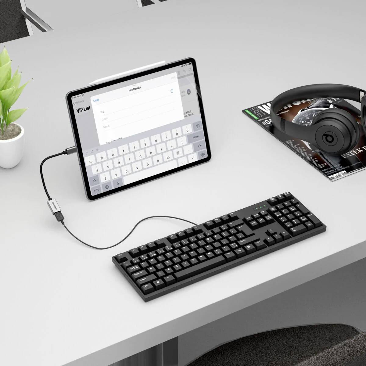 Une tablette avec un clavier affiché est connectée par un câble à un clavier physique. Un casque est posé à côté sur un magazine.