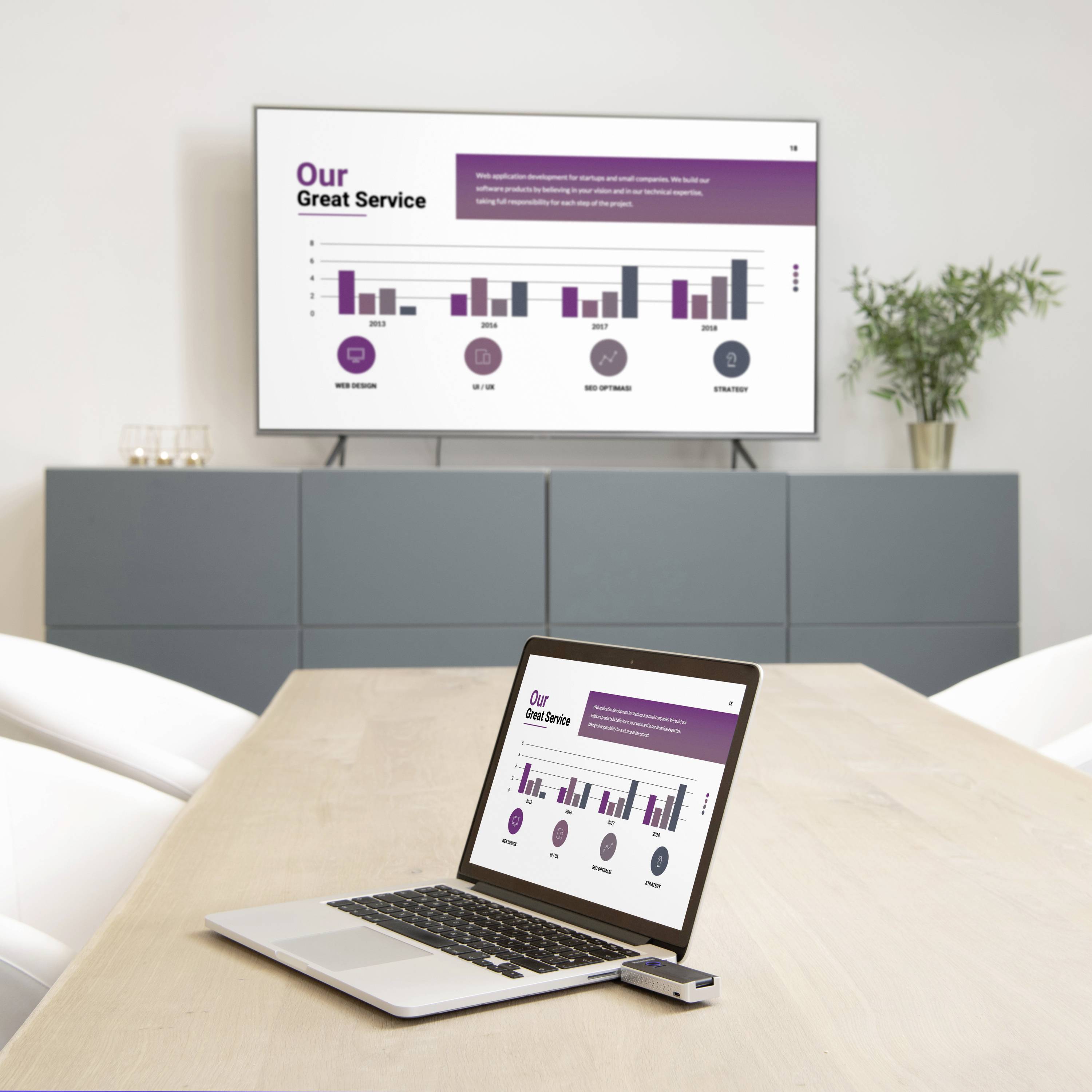 Sur une table, un ordinateur portable affiche un diagramme avec des barres et des cercles relatifs à un service. En arrière-plan, un diagramme similaire est visible sur un grand écran.