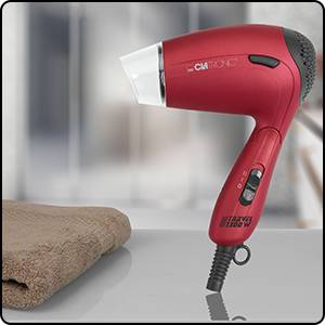 Un sèche-cheveux rouge avec une poignée noire est posé sur une surface lisse à côté d'une serviette pliée.