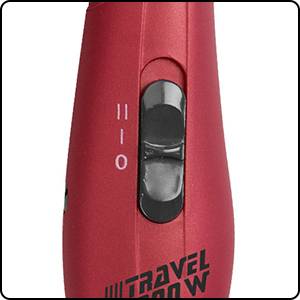 Un sèche-cheveux de voyage rouge avec un curseur noir pour les niveaux de réglage 0, 1, 2. En dessous, il est écrit « Travel 1200 W ».
