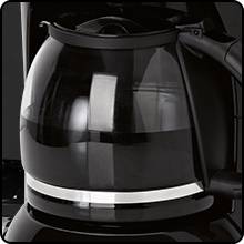 Un distributeur de café noir avec une carafe en verre remplie de café fraîchement brassé. La carafe reflète la lumière.