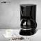 Machine à café avec carafe en verre sur un fond gris. À côté, une tasse de café est posée. Des grains de café sont éparpillés.