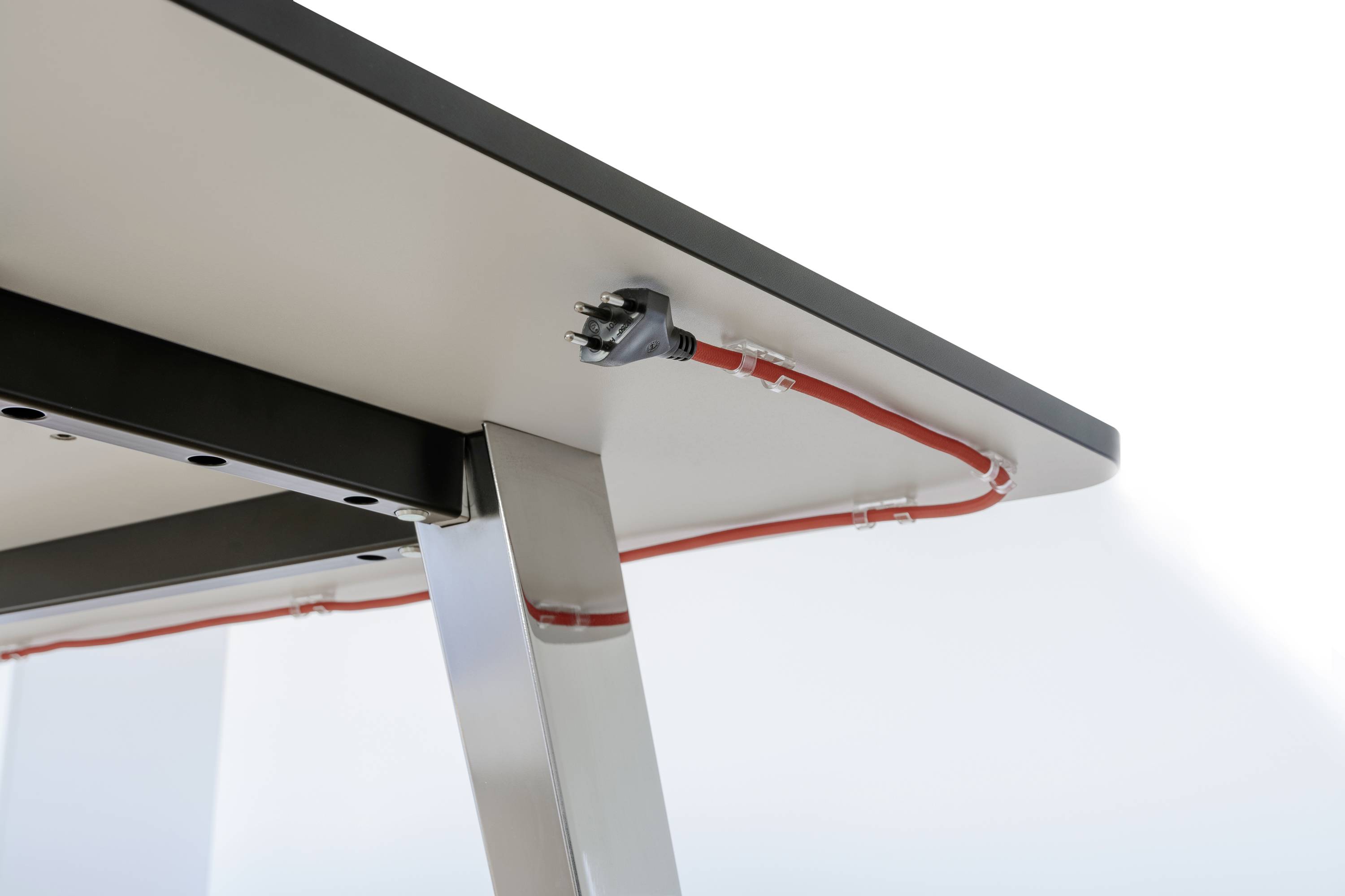 Prise électrique située sous la surface d'une table, avec le câble acheminé dans un chemin de câbles.