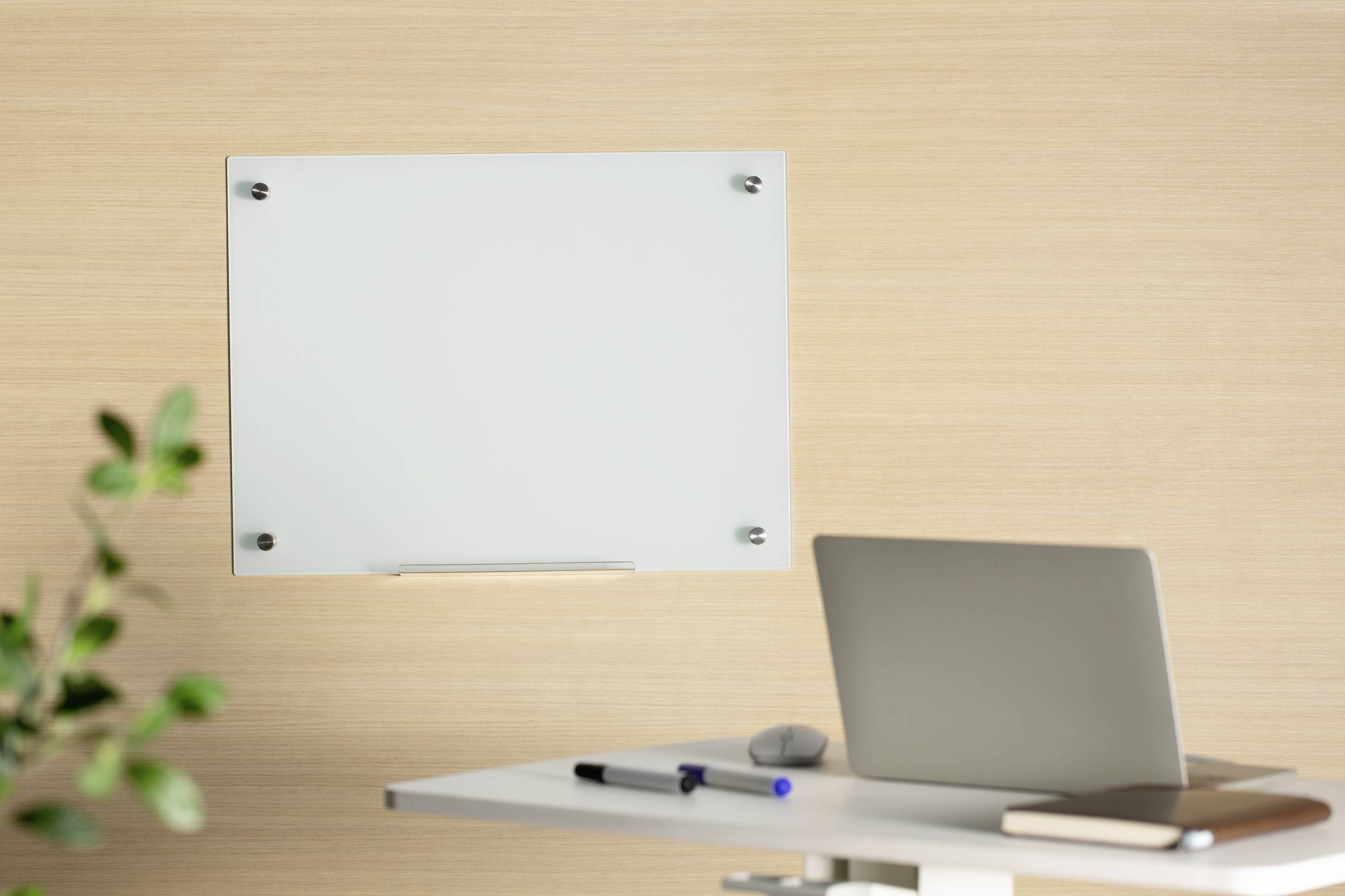 Un ordinateur portable et des ustensiles d'écriture sur un bureau devant un lambris en bois avec un tableau blanc vide au mur.