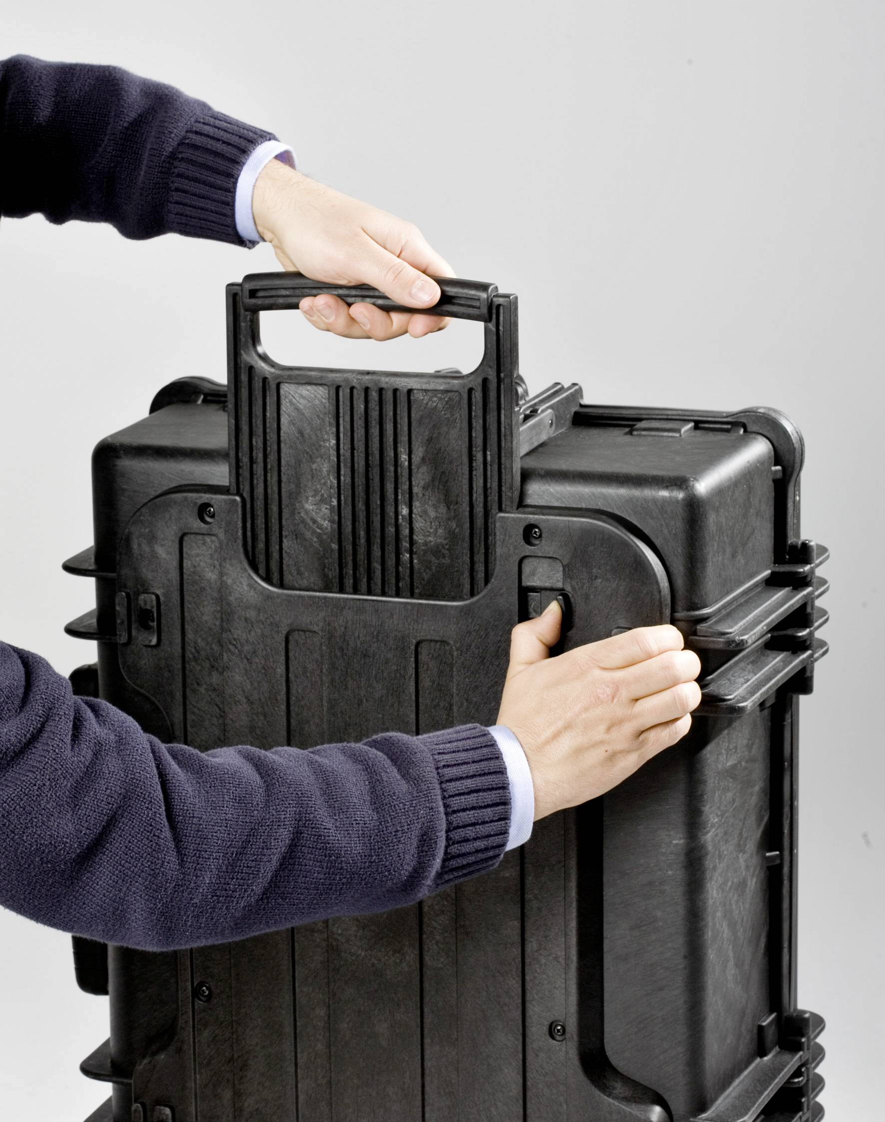 Une personne porte une grande valise noire avec une poignée robuste.