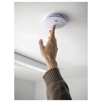 Main appuyant sur le bouton de test d'un détecteur de fumée montré au plafond.