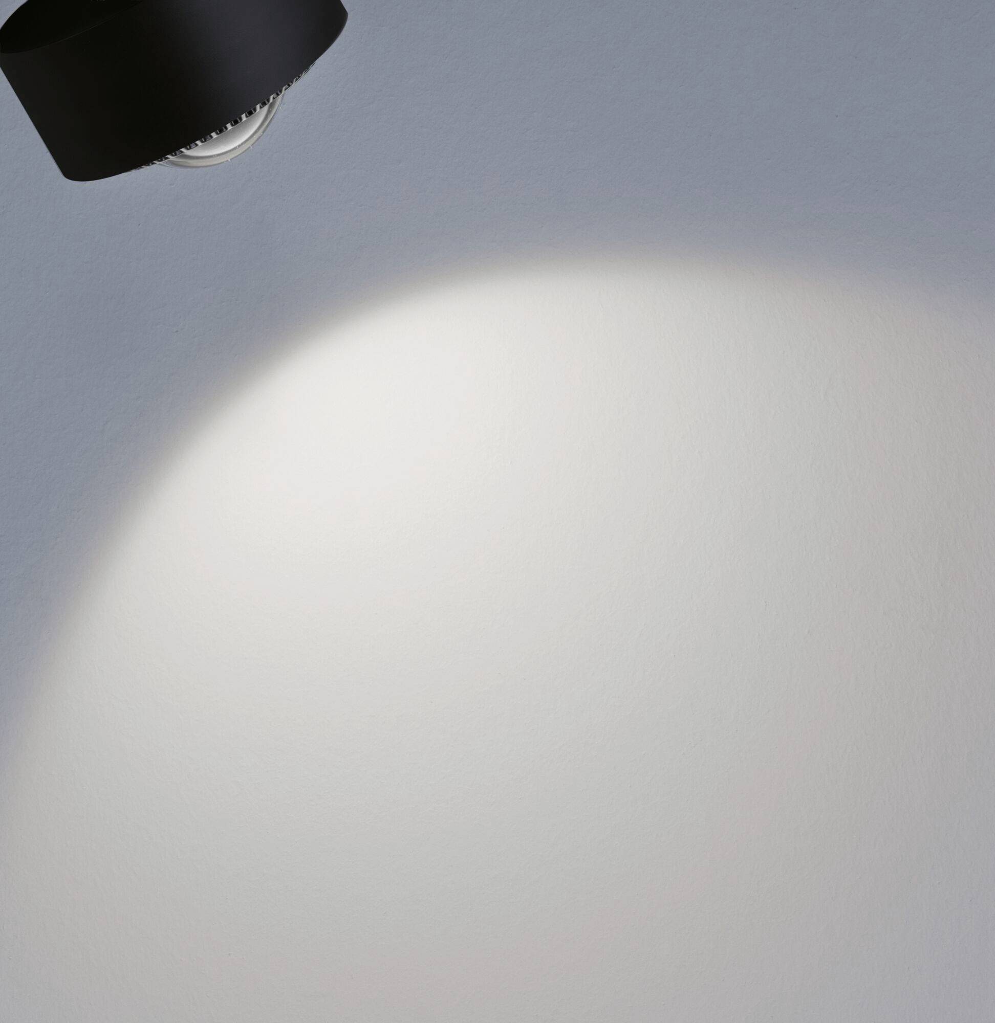 Un projecteur au plafond illumine une zone circulaire sur un mur gris, le reste restant dans l'ombre.