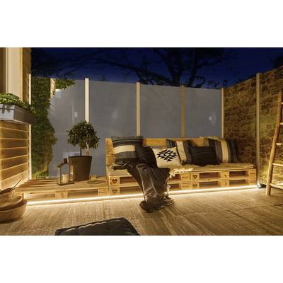 Salon cosy et éclairé à l'extérieur avec des meubles en palettes, des coussins et des couvertures sur une terrasse la nuit.