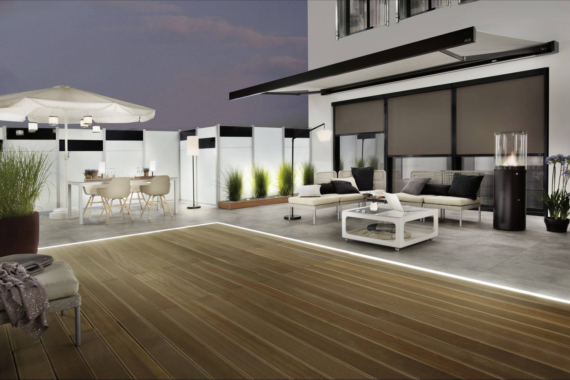Grande terrasse moderne sur le toit au crépuscule avec un sol en bois, des meubles de salon, une table à manger et un éclairage. Idéal pour se détendre et se réunir.