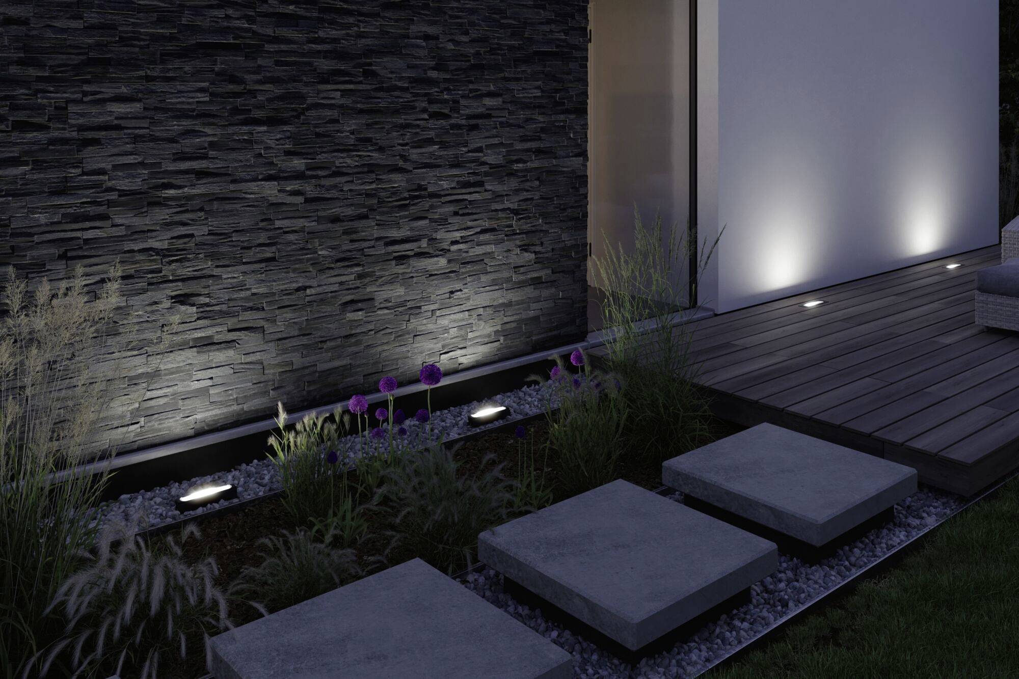 Un jardin au design contemporain, avec des dalles de béton éclairées menant à l'entrée principale. À gauche, un mur de pierre est illuminé.