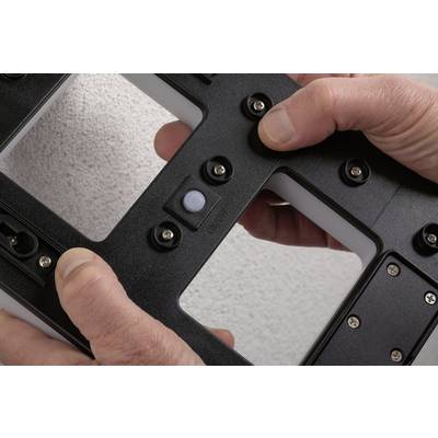 Deux mains tiennent un appareil noir rectangulaire avec plusieurs vis argentées et un capteur blanc au centre.