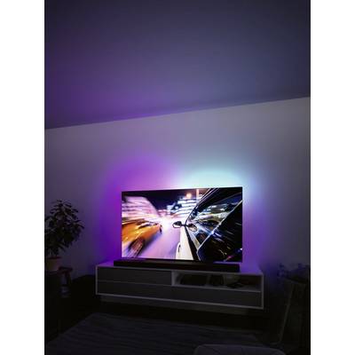 Un téléviseur moderne affiche une course nocturne aux couleurs vives, reflétant la lumière dans la pièce, et est posé sur une étagère blanche.