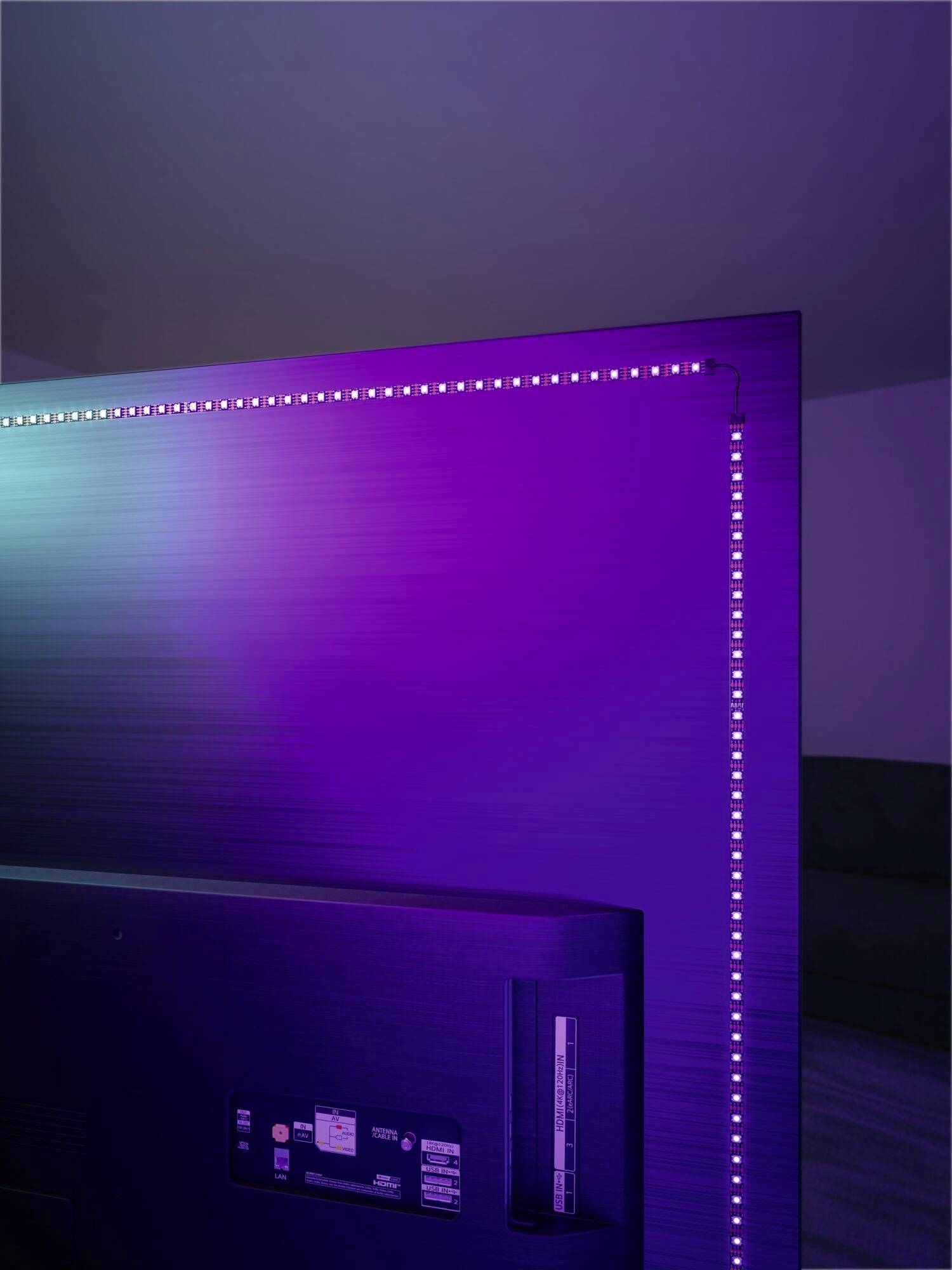 Vue arrière d'un téléviseur avec des LED violettes disposées le long des bords. Pièce ambiancée avec un éclairage d'atmosphère.