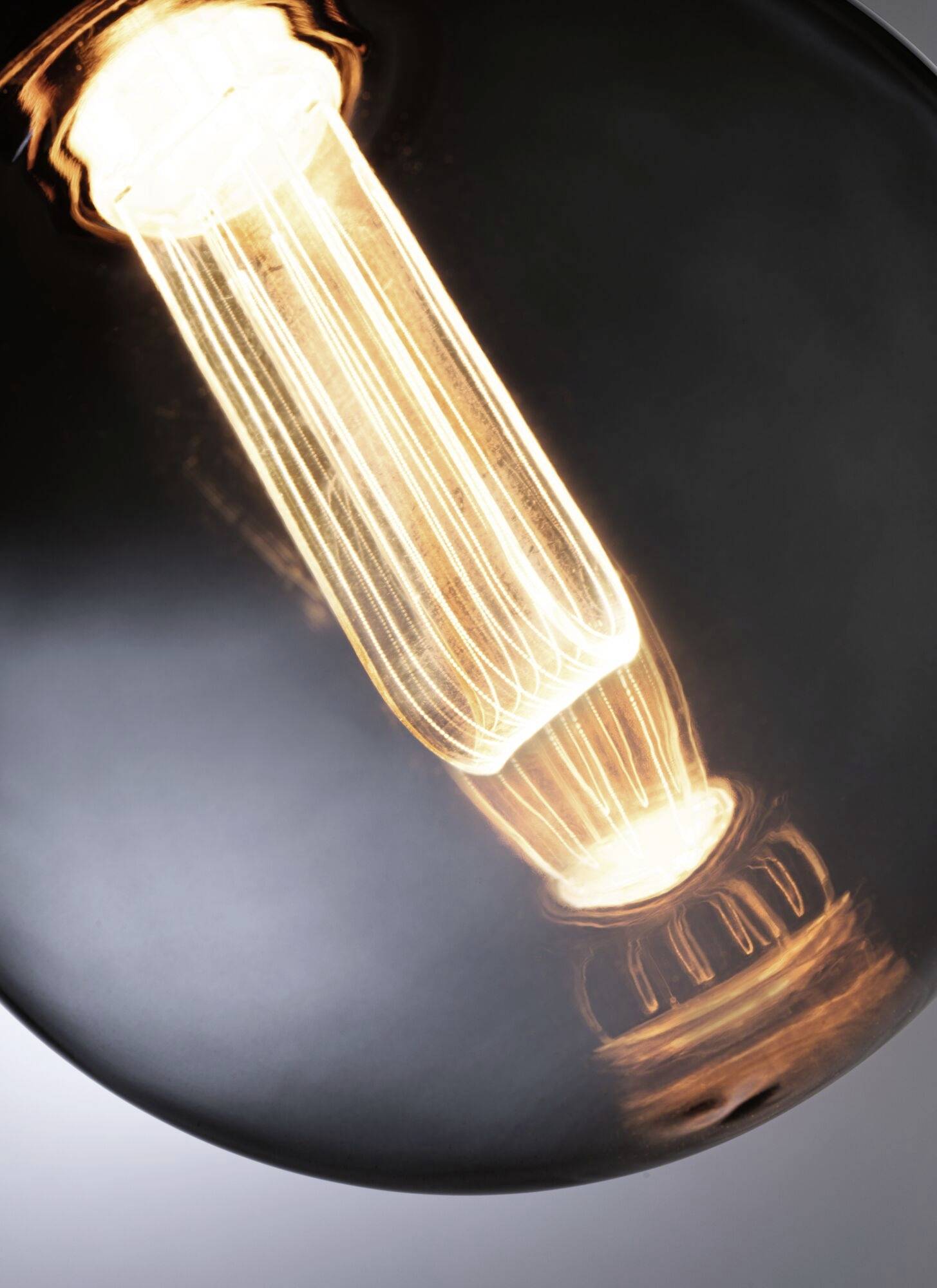 Gros plan d'une ampoule allumée avec des filaments visibles émettant une lumière chaude.