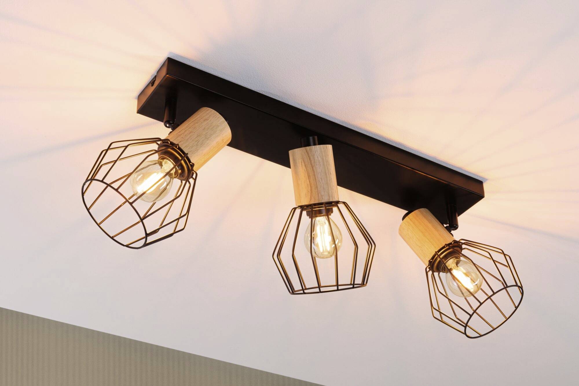 Trois luminaires suspendus au design en bois et en fil métallique diffusent une lumière chaleureuse ; ils sont installés dans un intérieur moderne.