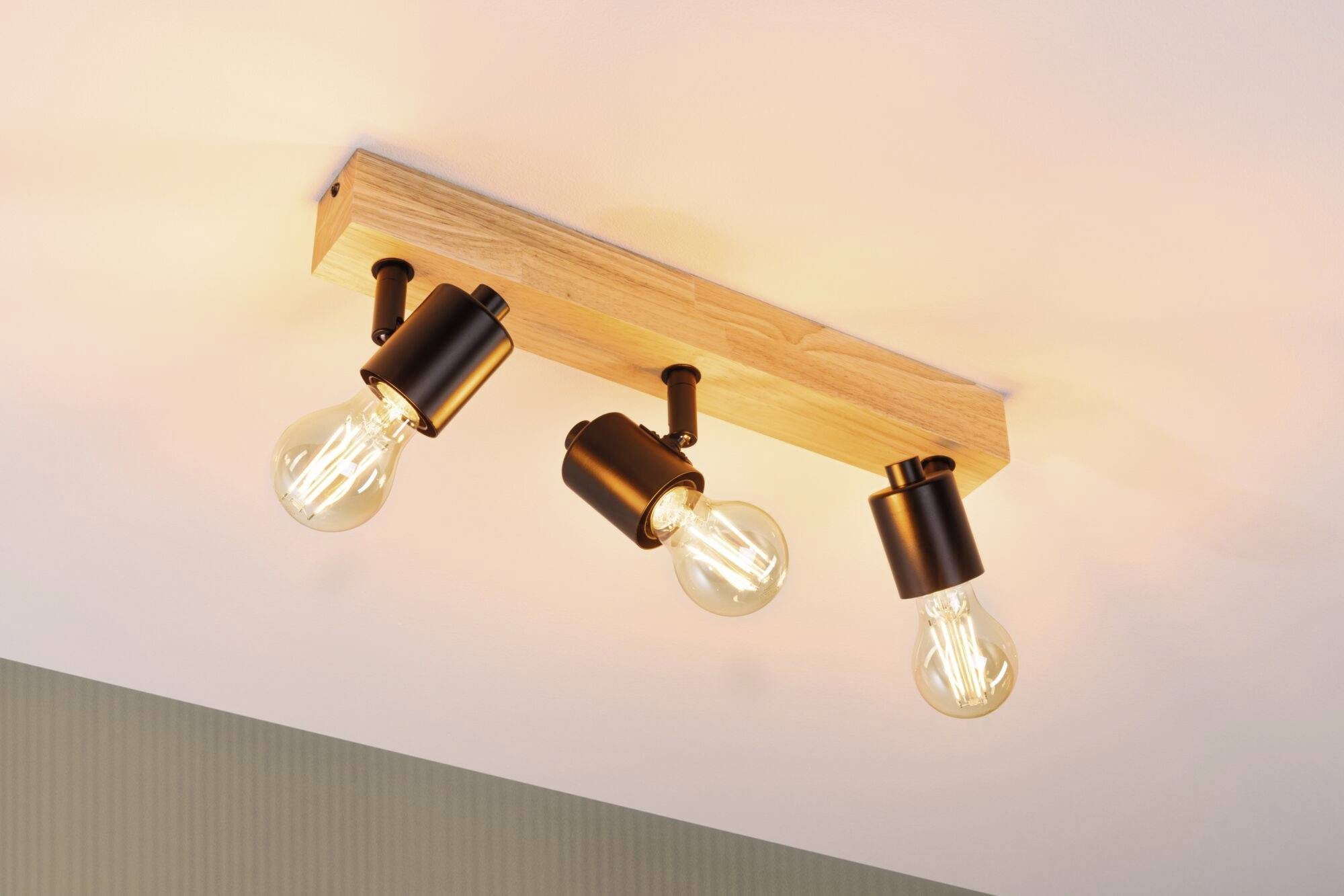 Trois luminaires noirs suspendus dans un cadre rectangulaire en bois émettent une lumière chaleureuse et illuminent la pièce depuis le plafond.