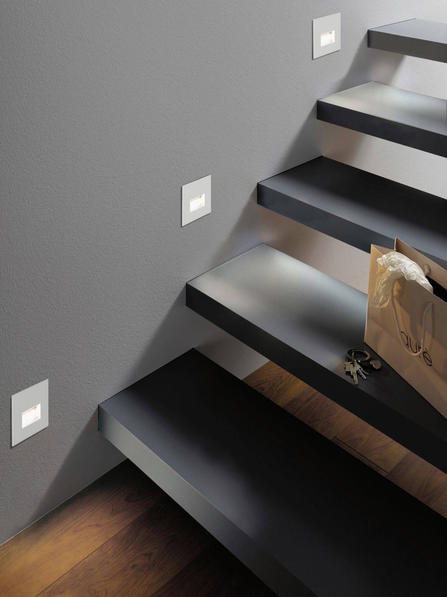 Un escalier au design moderne avec des lumières latérales. Un sac de courses marron et un trousseau de clés sont posés sur une marche.