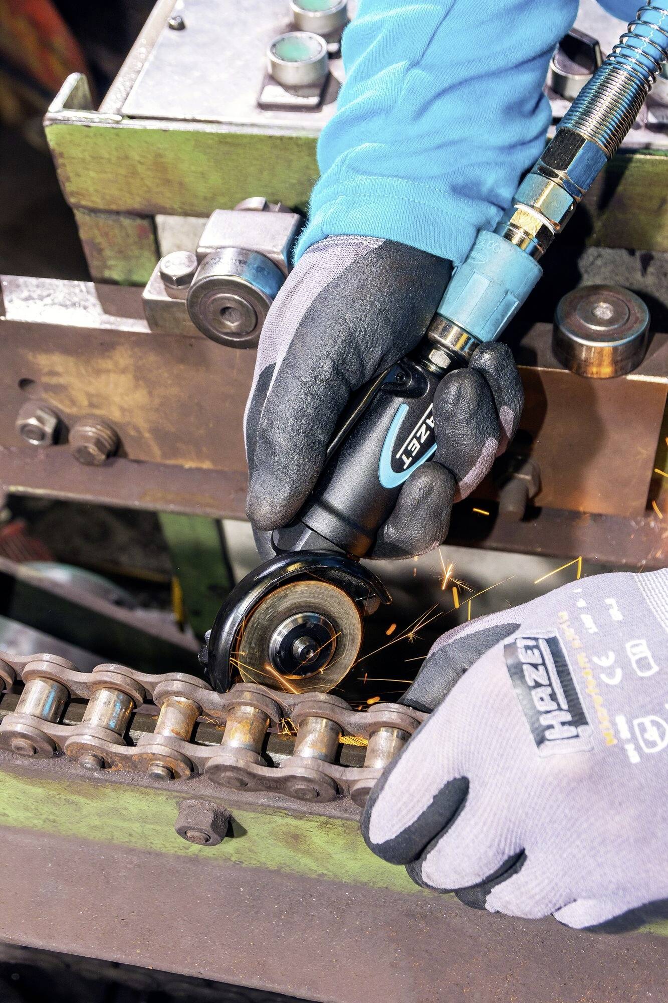 Une personne meule du métal sur une machine à l'aide d'une meuleuse d'angle. Des étincelles volent. La personne porte des gants de protection bleus et gris.