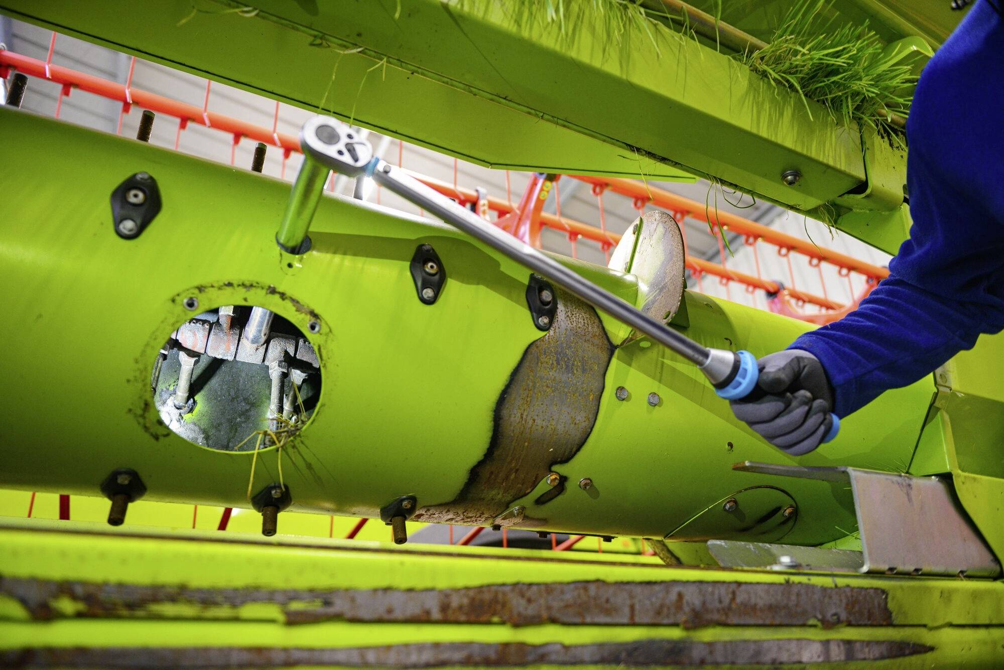 Un mécanicien utilise une clé dynamométrique pour réparer un engin agricole vert dans un atelier.