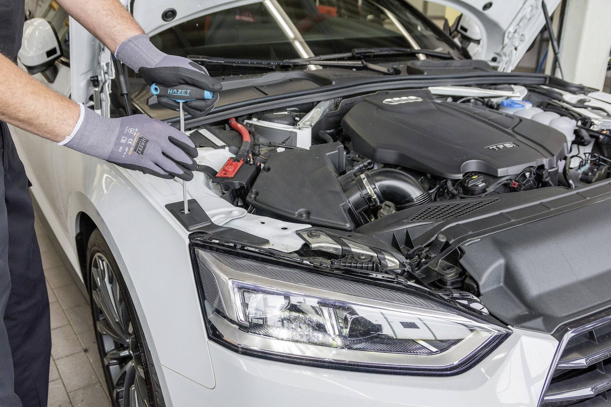 Un mécanicien travaille avec un tournevis sur le moteur d'une voiture blanche décapotable dans un atelier.