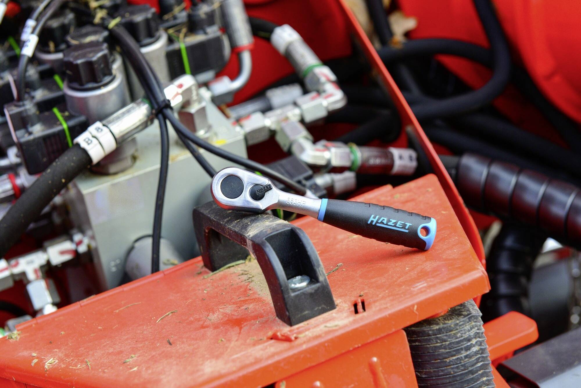 Une clé à molette est posée sur une machine rouge avec plusieurs câbles et tuyaux. L'outil est utilisé pour la maintenance ou la réparation.