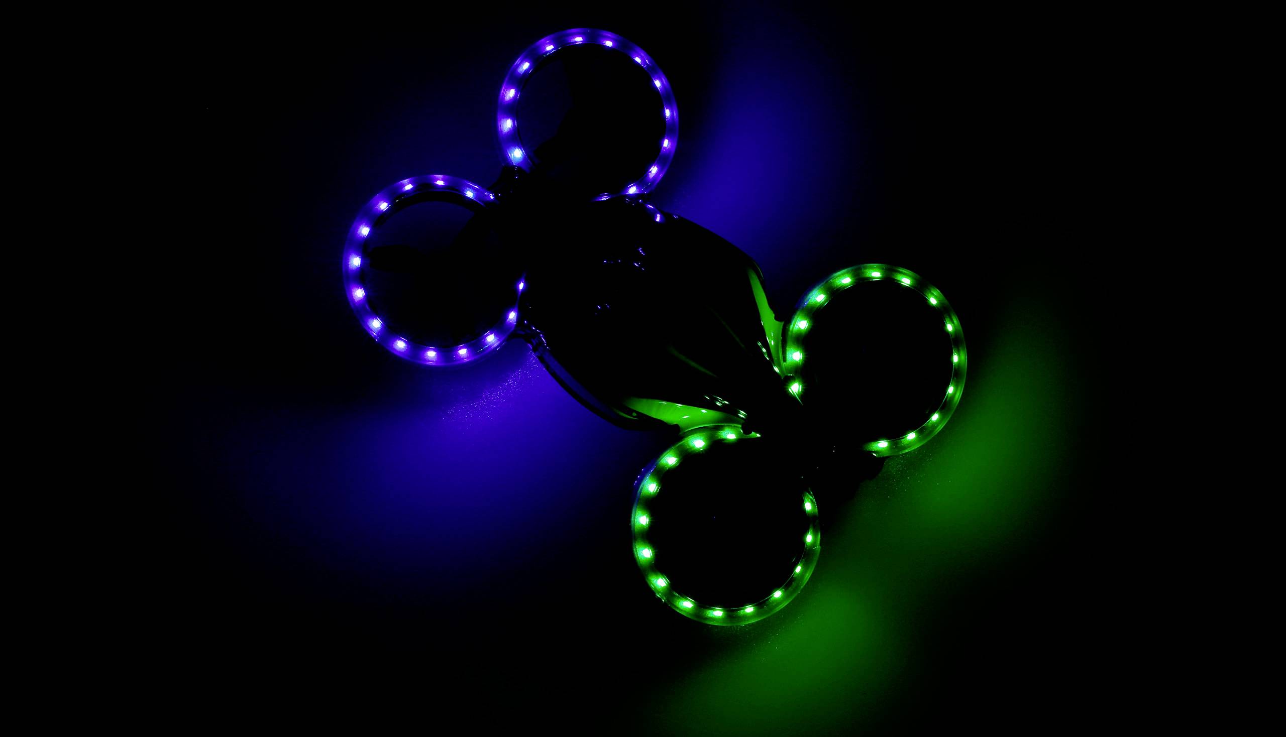 Drone avec des lumières bleues et vertes brillantes volant dans l'obscurité.