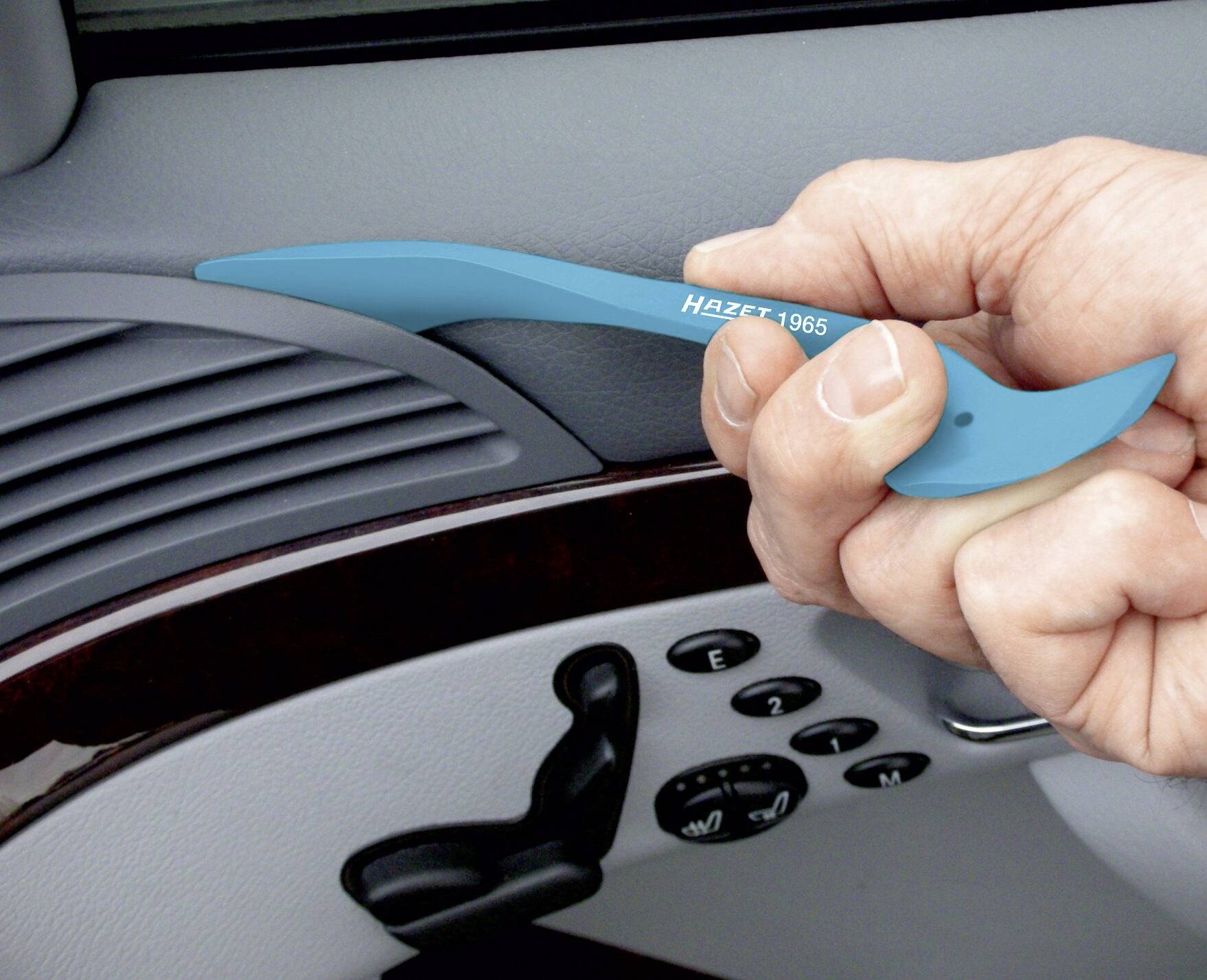 Une main tient un outil en plastique bleu pour retirer le revêtement intérieur d'une fenêtre de voiture. Des détails du tableau de bord sont visibles en arrière-plan.