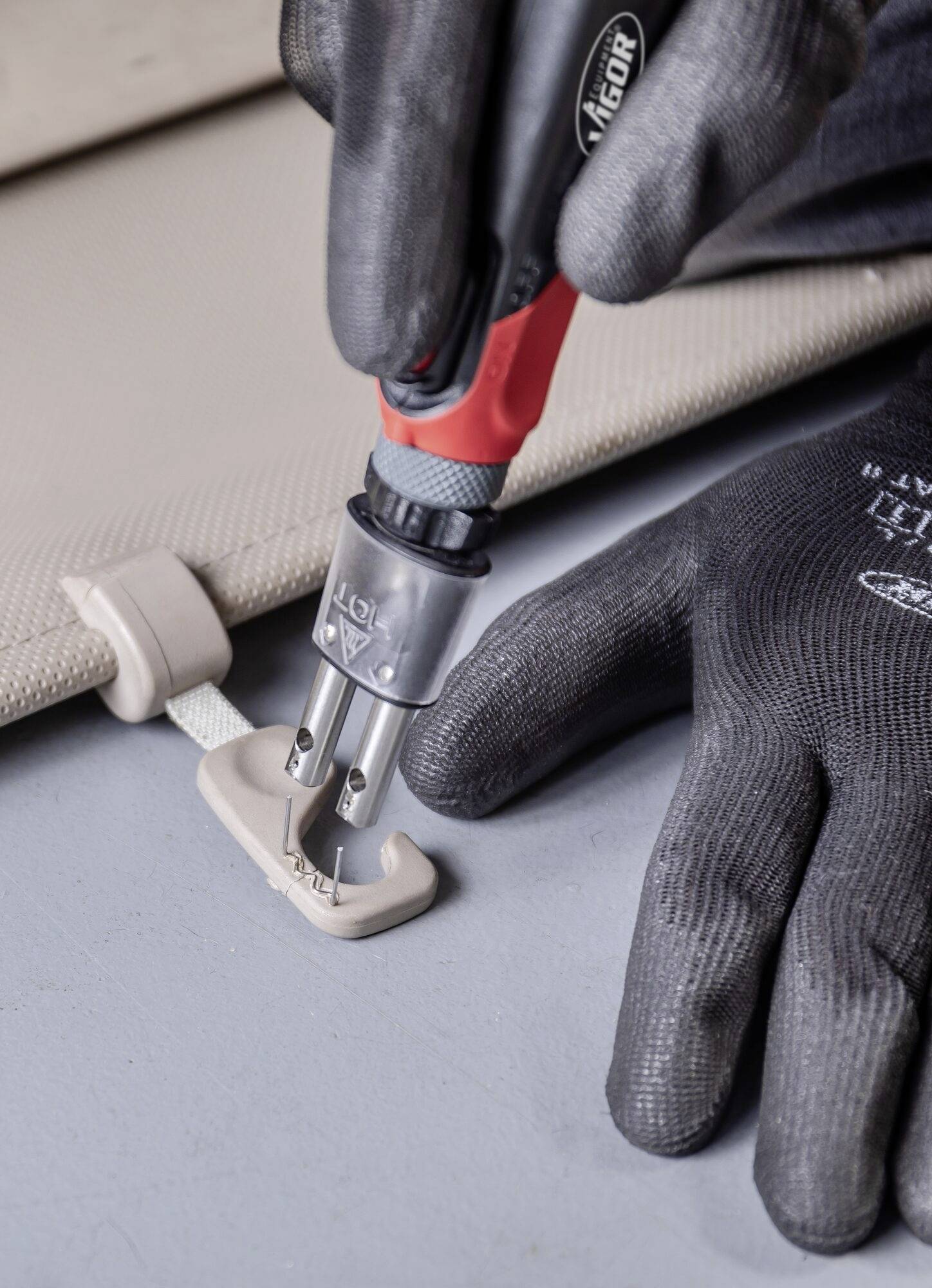 Une personne portant des gants noirs fixe un petit support sur une surface à l'aide d'un tournevis rouge.