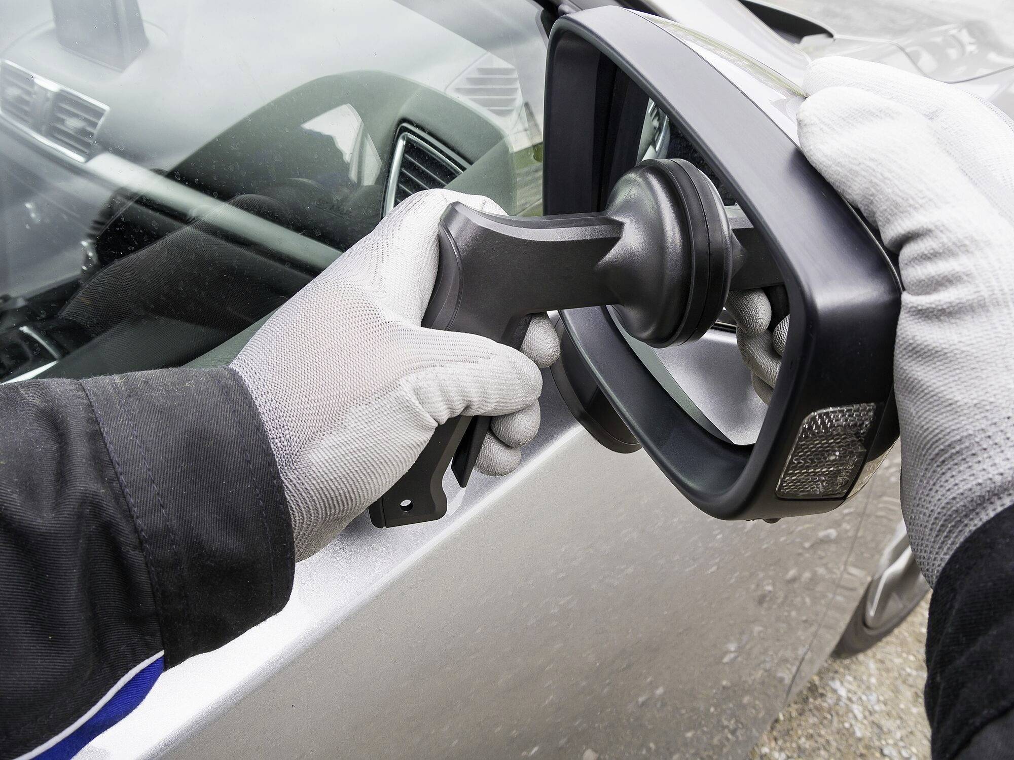 Une main dans un gant tient une prise de charge connectée à une voiture électrique. Reflétée dans le rétroviseur latéral du véhicule.