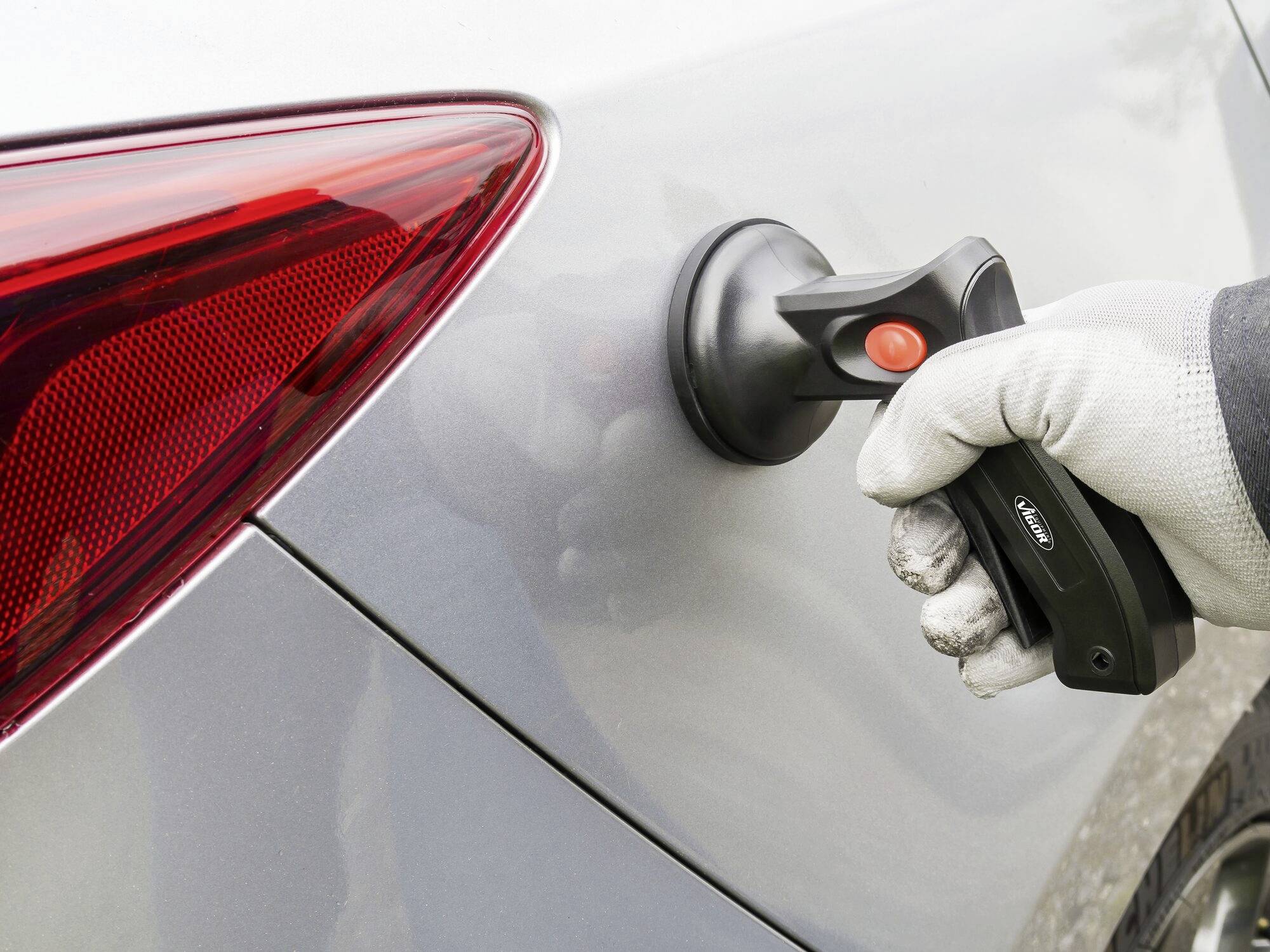 Une personne polit la carrosserie d'une voiture argentée à l'aide d'un appareil électrique, reconnaissable au niveau du phare arrière.