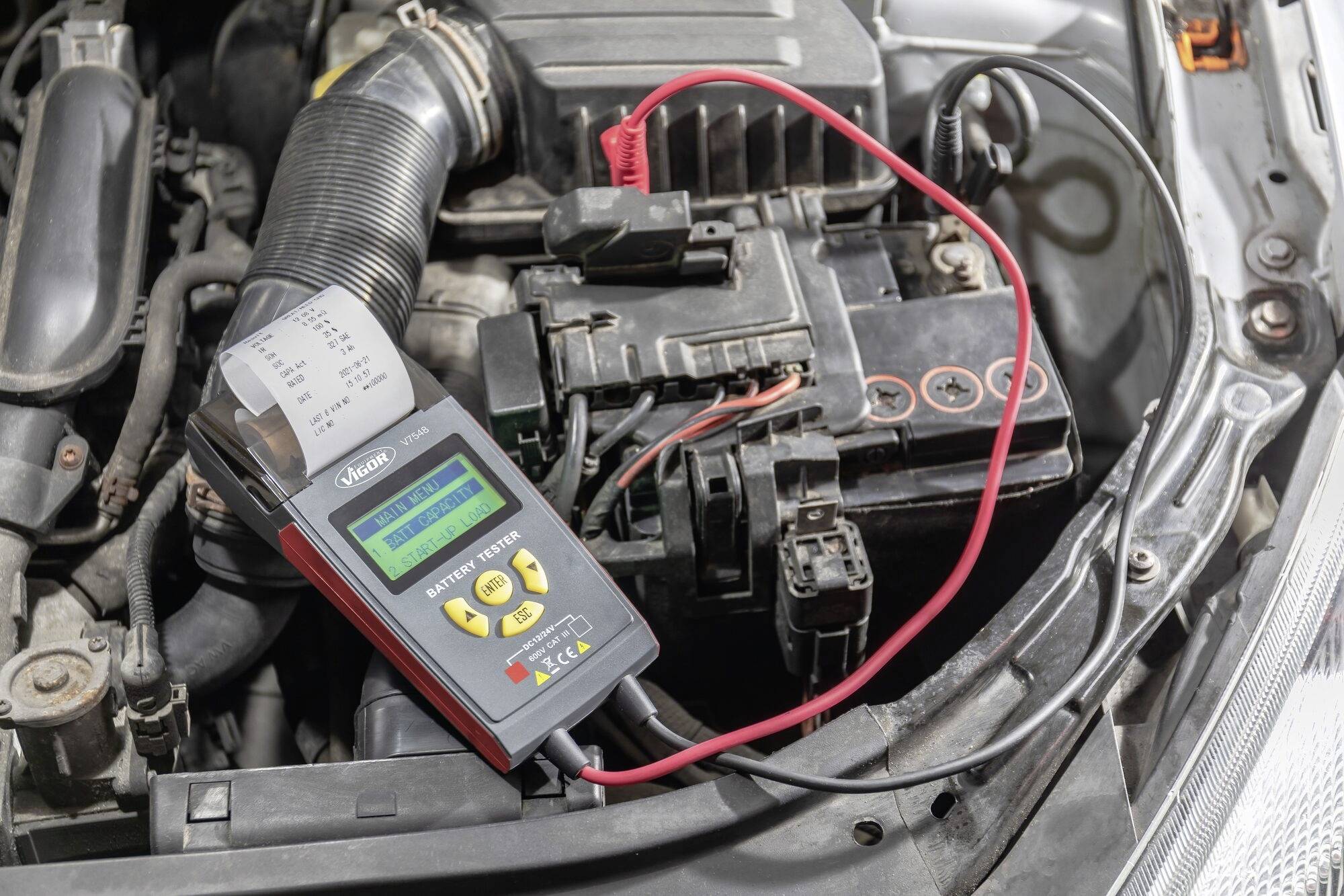 Appareil de diagnostic électronique mesurant la tension de la batterie de voiture dans le compartiment moteur ouvert. Les câbles rouge et noir sont connectés.