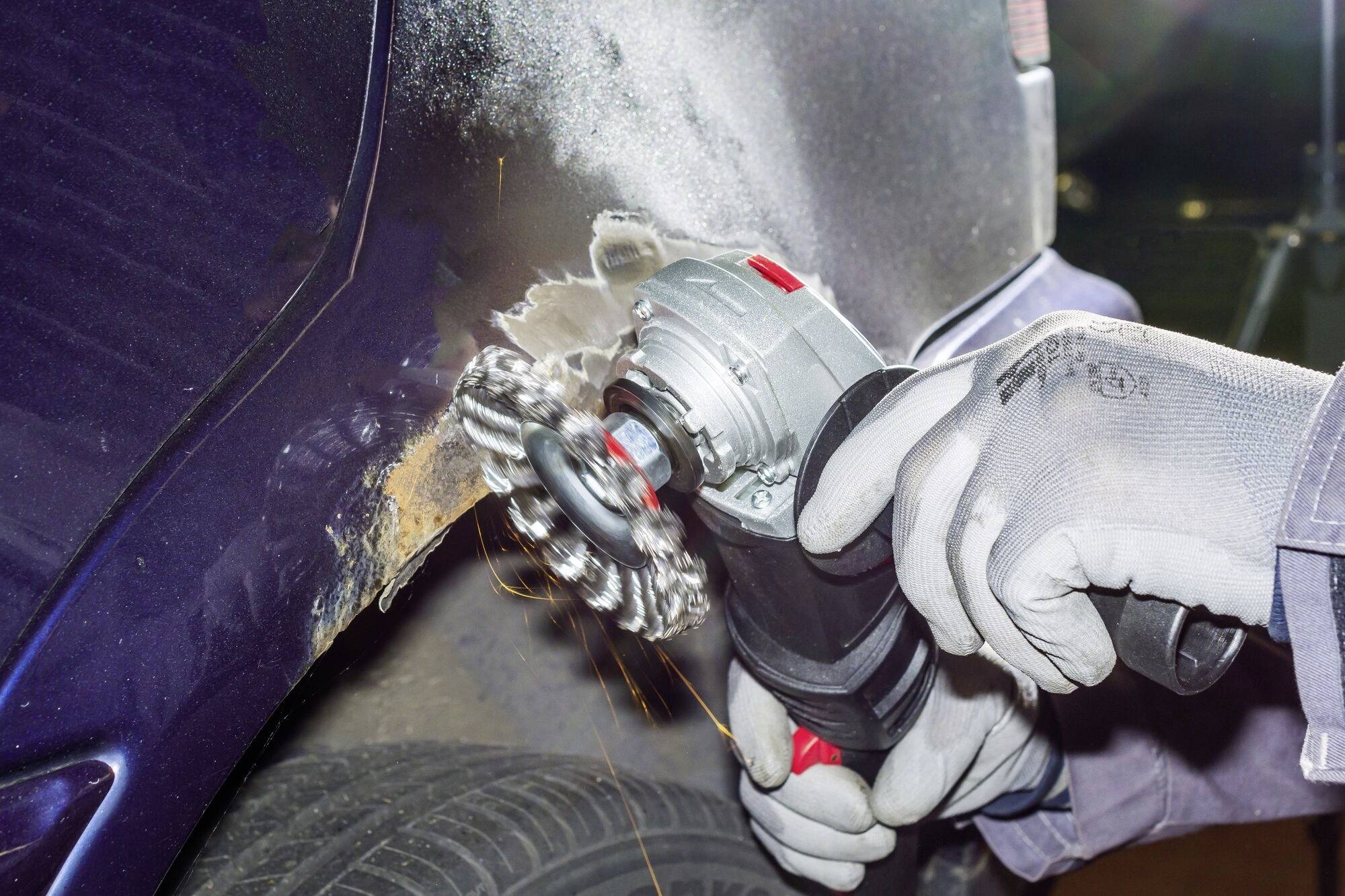 Une personne retire la rouille d'un aile de voiture à l'aide d'une meuleuse d'angle. Des étincelles jaillissent pendant que le métal est travaillé.
