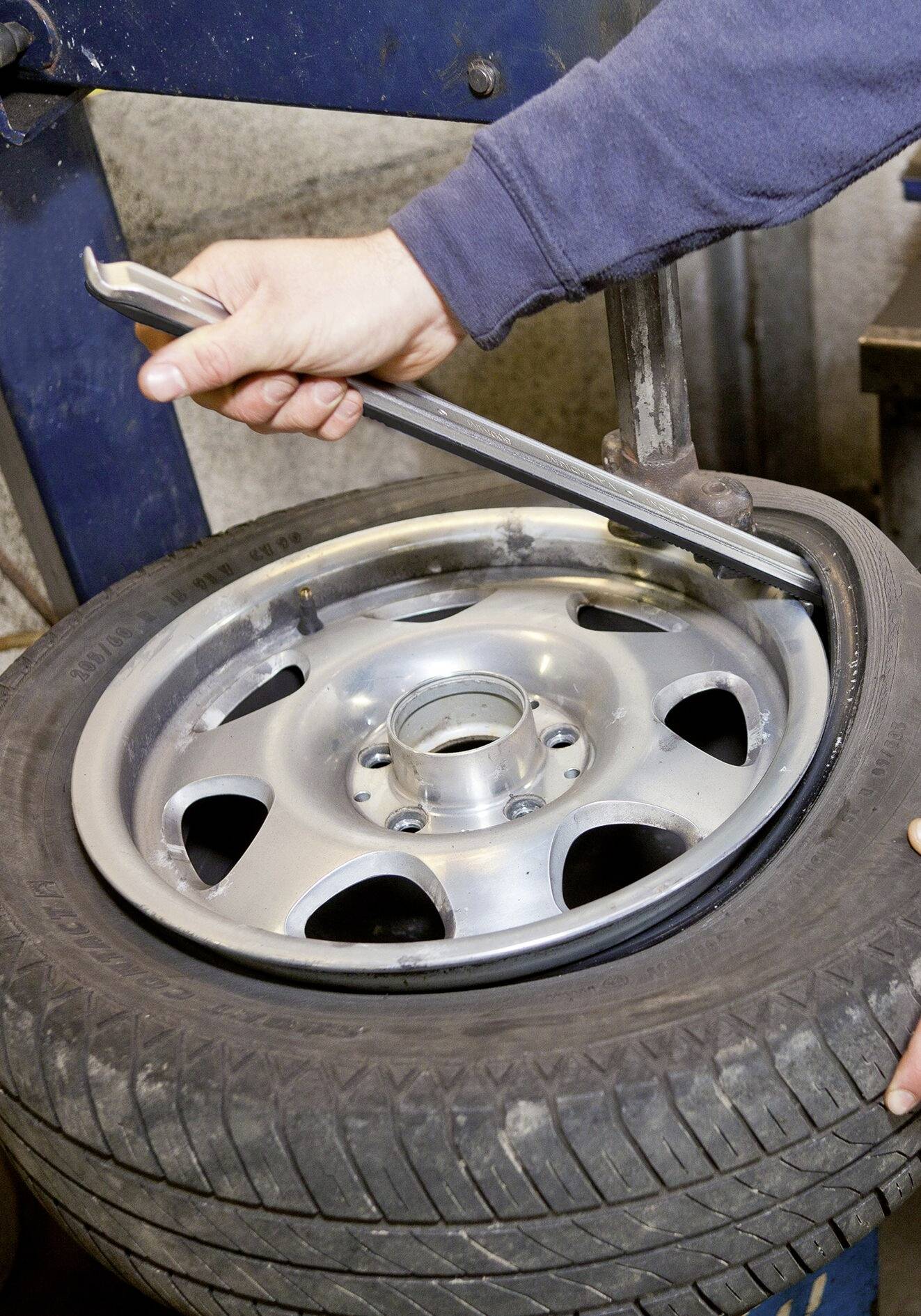 Une personne installe un pneu sur une jante à l'aide d'un outil de levage dans un environnement d'atelier.