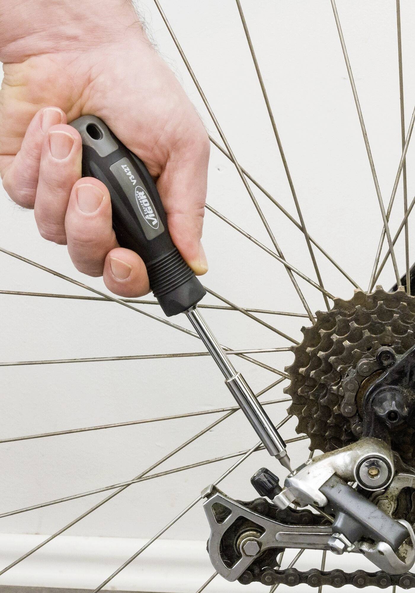 Une main ajuste un dérailleur de vélo avec un tournevis, avec un focus sur les pignons et l'outil en action.