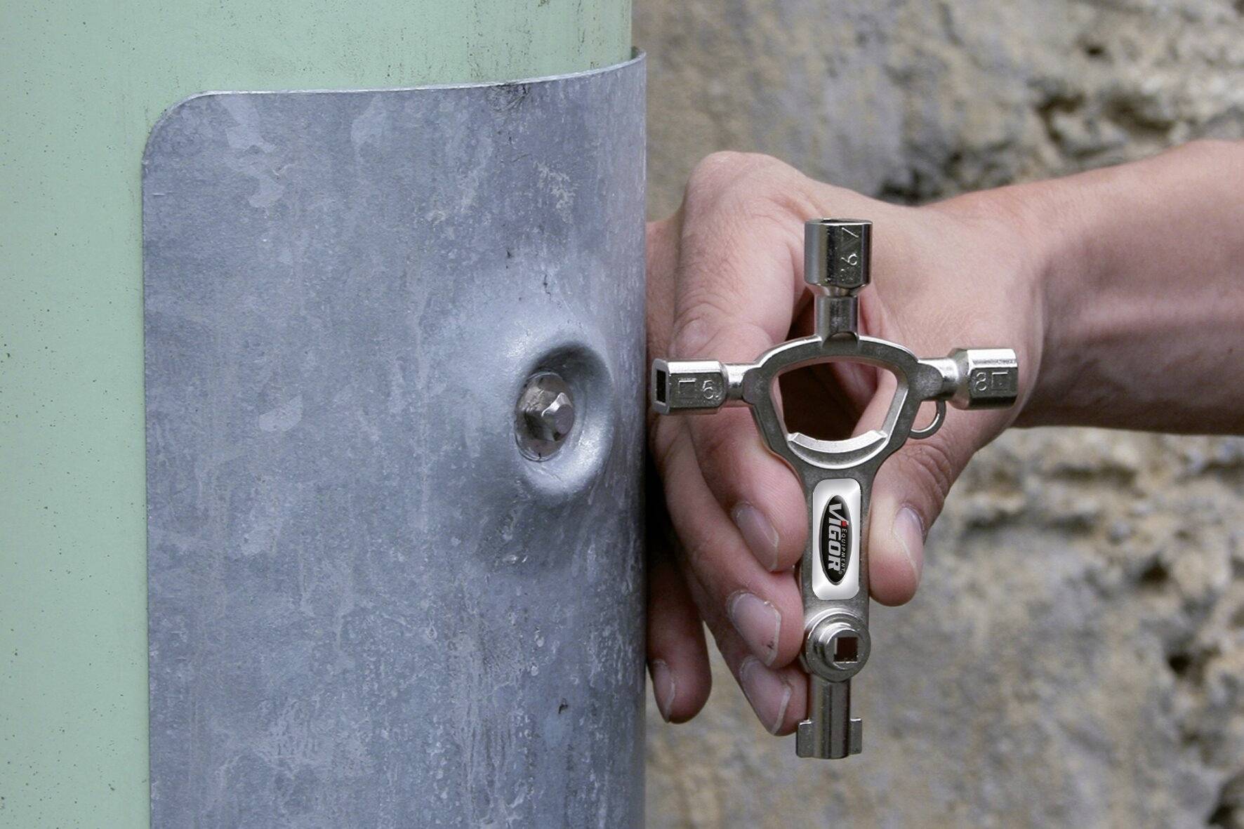 Une main utilise un outil multifonction avec différentes formes de clés pour dévisser une vis sur une plaque métallique.