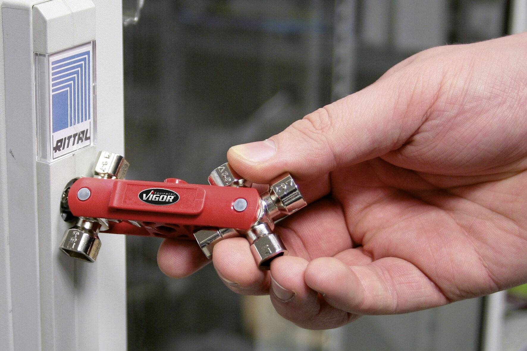 Une main tient un outil rouge avec plusieurs clés devant une porte d'armoire portant le logo 'Rittal'.