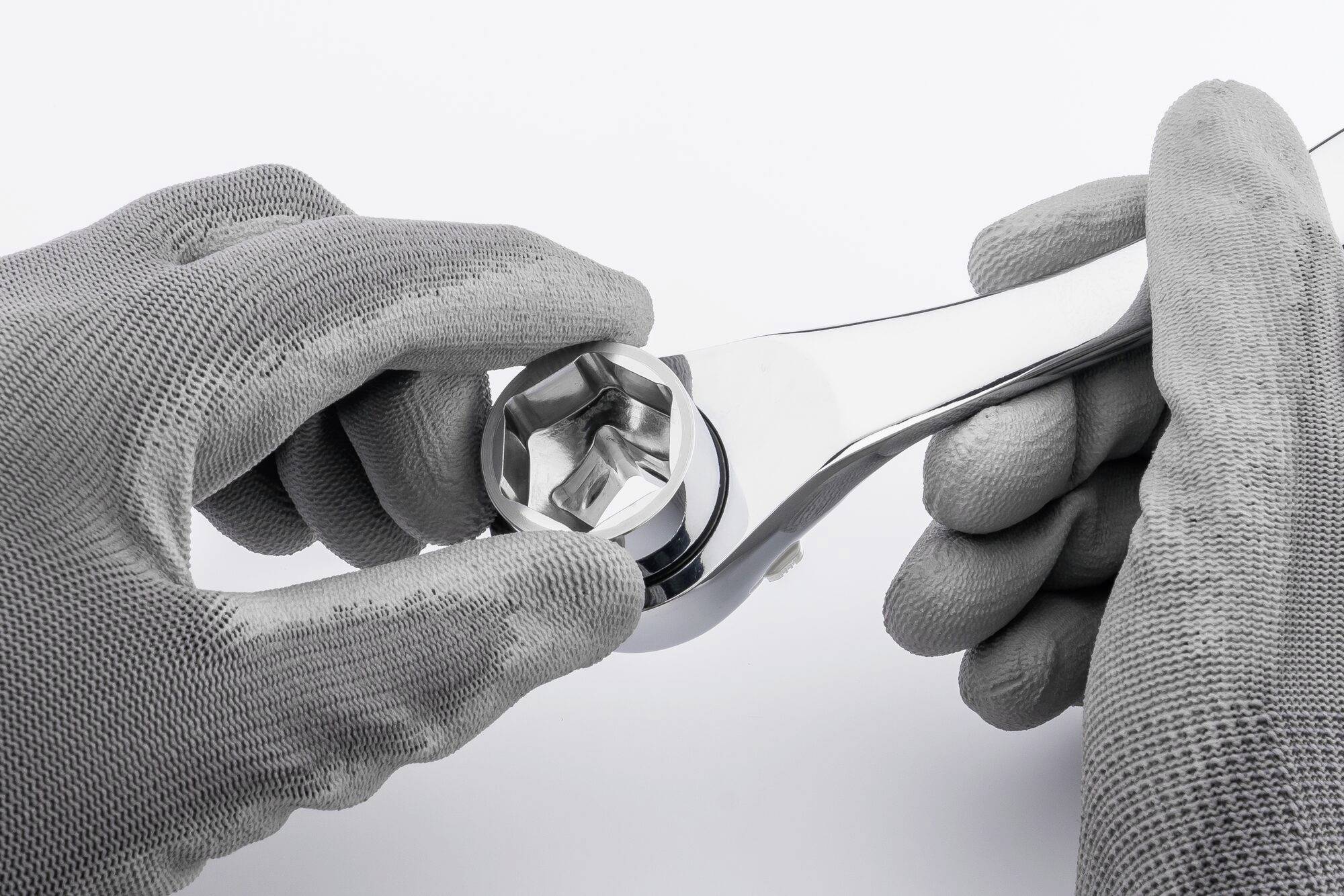 Deux mains grises gantées tiennent une clé à molette chromée avec un mécanisme à cliquet, prêtes à travailler sur une vis.