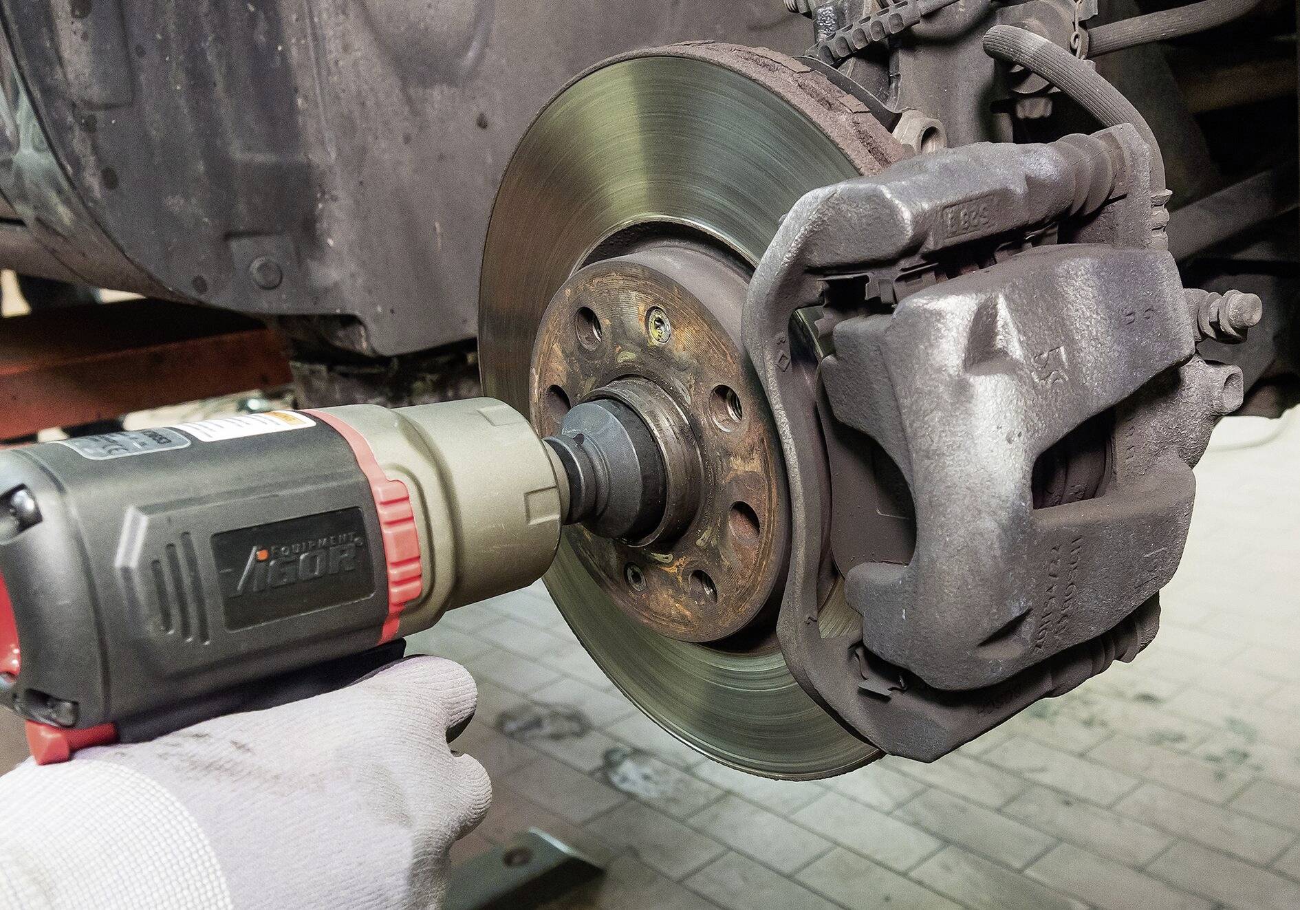 Un mécanicien utilise une visseuse à choc pour fixer un écrou de roue sur le disque de frein d'une voiture dans un atelier.