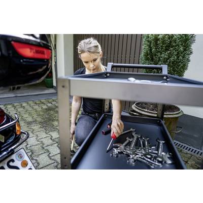 Une personne organise des outils sur un chariot roulant à côté d'une voiture dans un garage. Elle tient un tournevis.