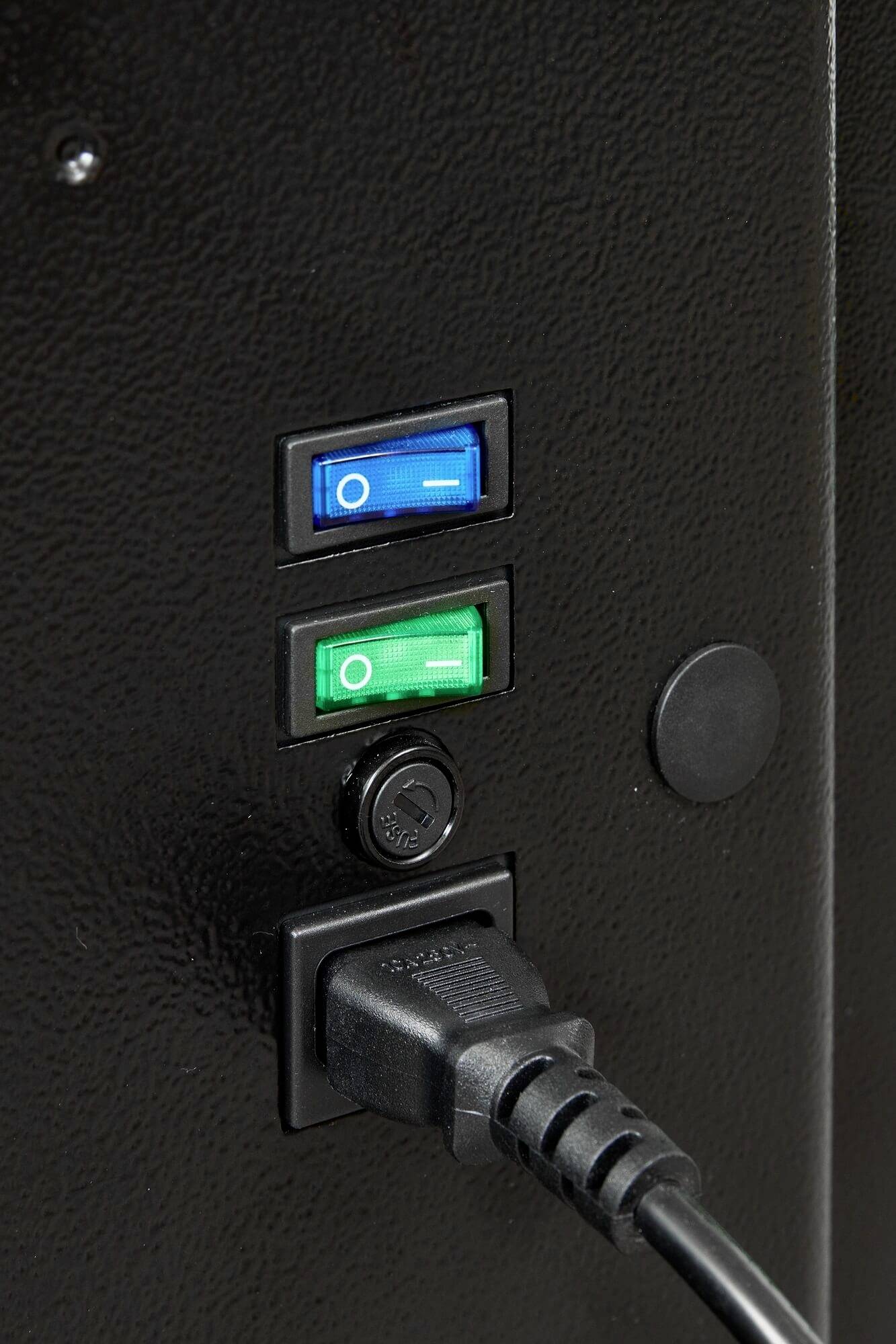 Un appareil noir avec un interrupteur à bascule bleu et vert qui est illuminé. Un câble est branché dans une prise électrique située en dessous.