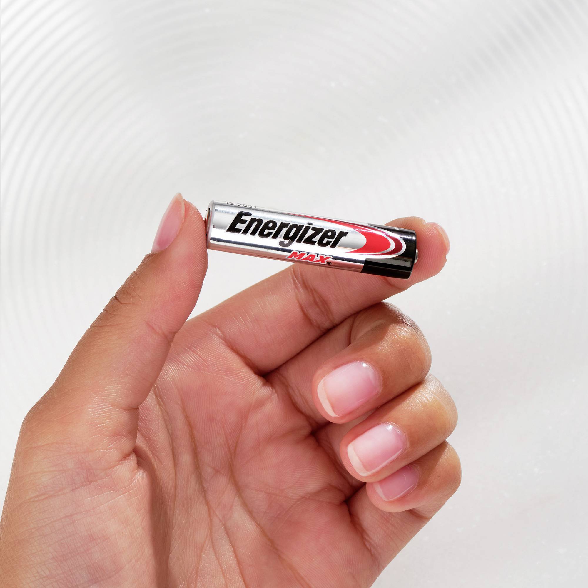 Une main tient une pile AA de la marque Energizer Max devant un arrière-plan lumineux flou.