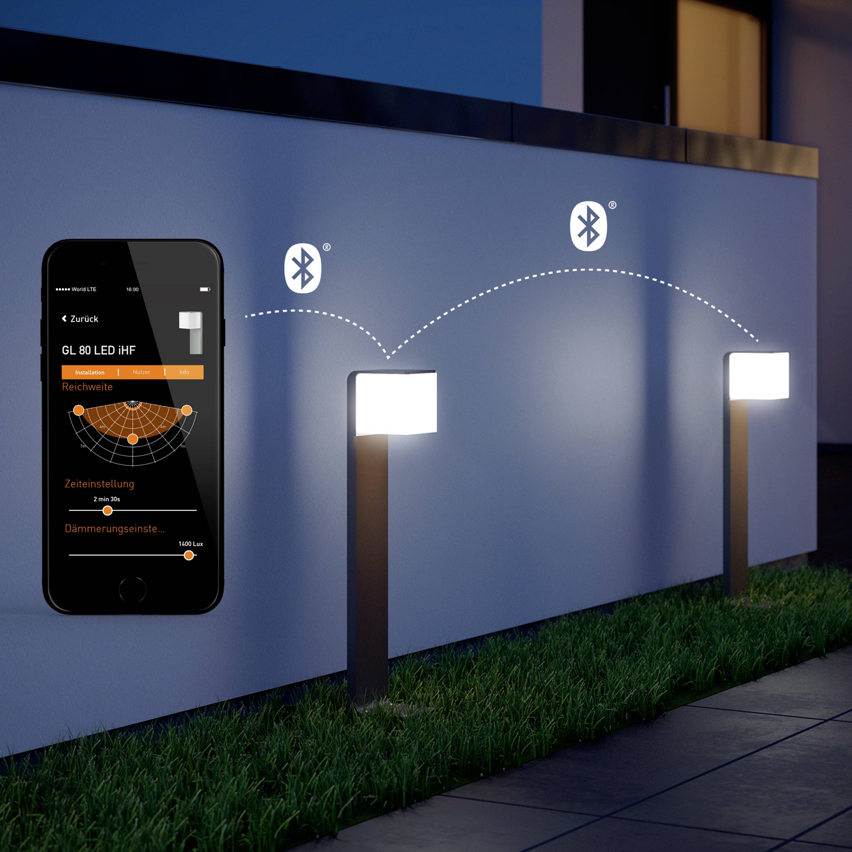 Un smartphone affiche des paramètres pour contrôler des luminaires de jardin LED via Bluetooth, situés à côté d'un chemin éclairé.