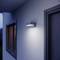 Un luminaire moderne fixé au mur de la maison éclaire doucement les alentours au crépuscule.