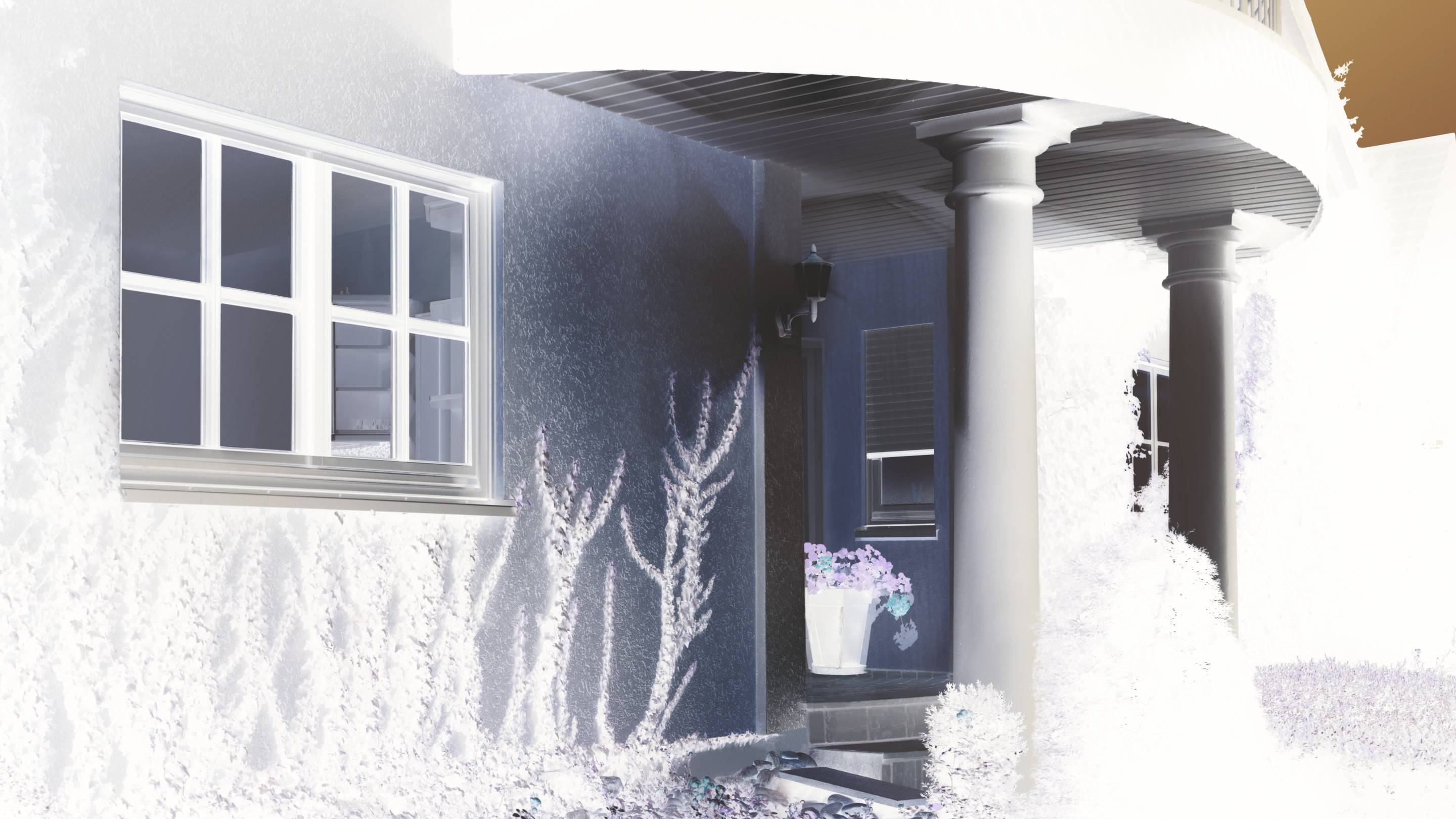 Entrée d'une maison avec deux colonnes et une porte. À côté se trouve une fenêtre. Des plantes et des fleurs décorent la zone.