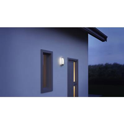 Une lampe extérieure brille à côté d'une porte et d'une fenêtre sur une maison au crépuscule.