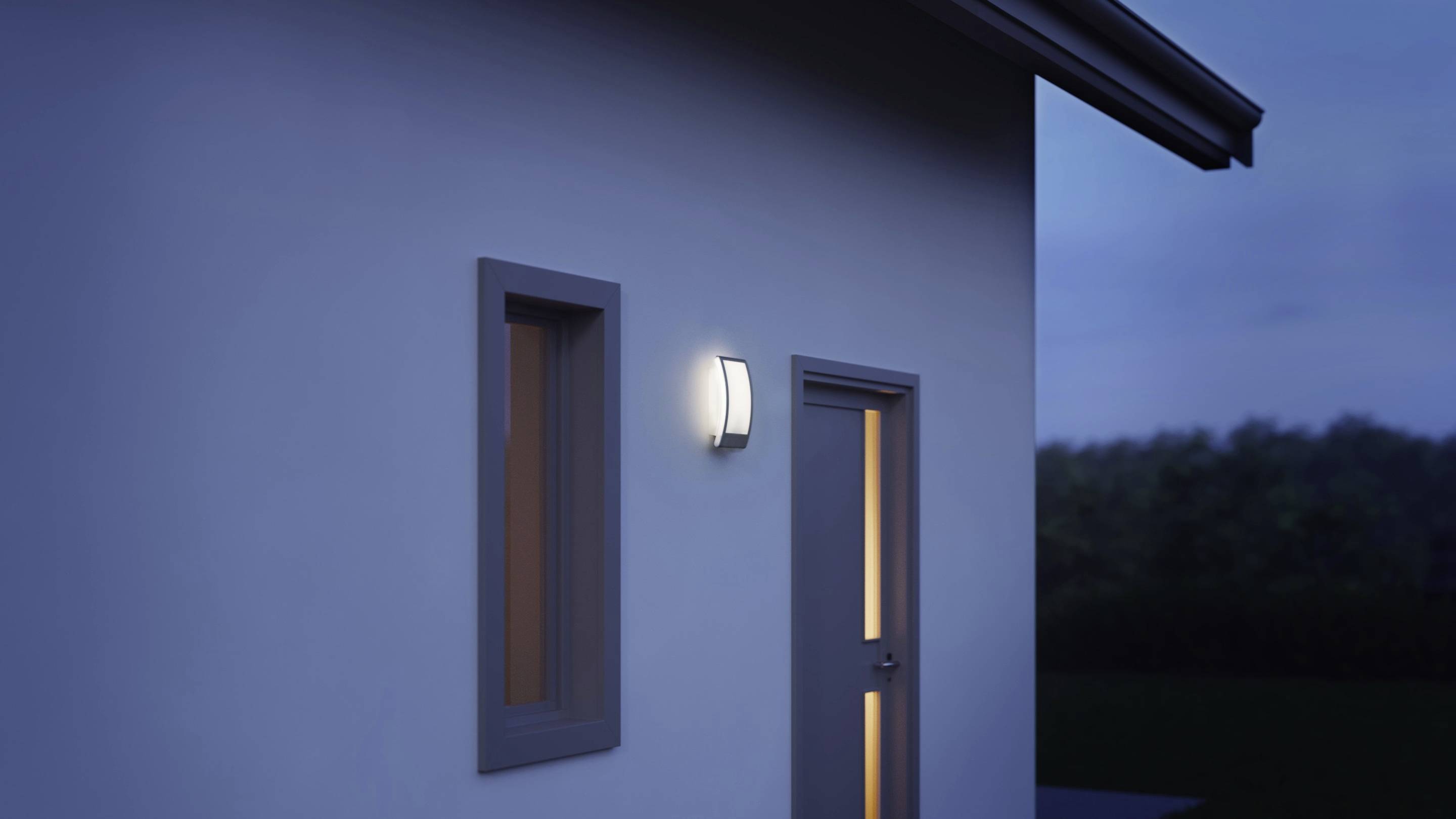 Éclairage extérieur illuminé sur un mur de maison au crépuscule, à côté d'une fenêtre fermée et d'une porte.